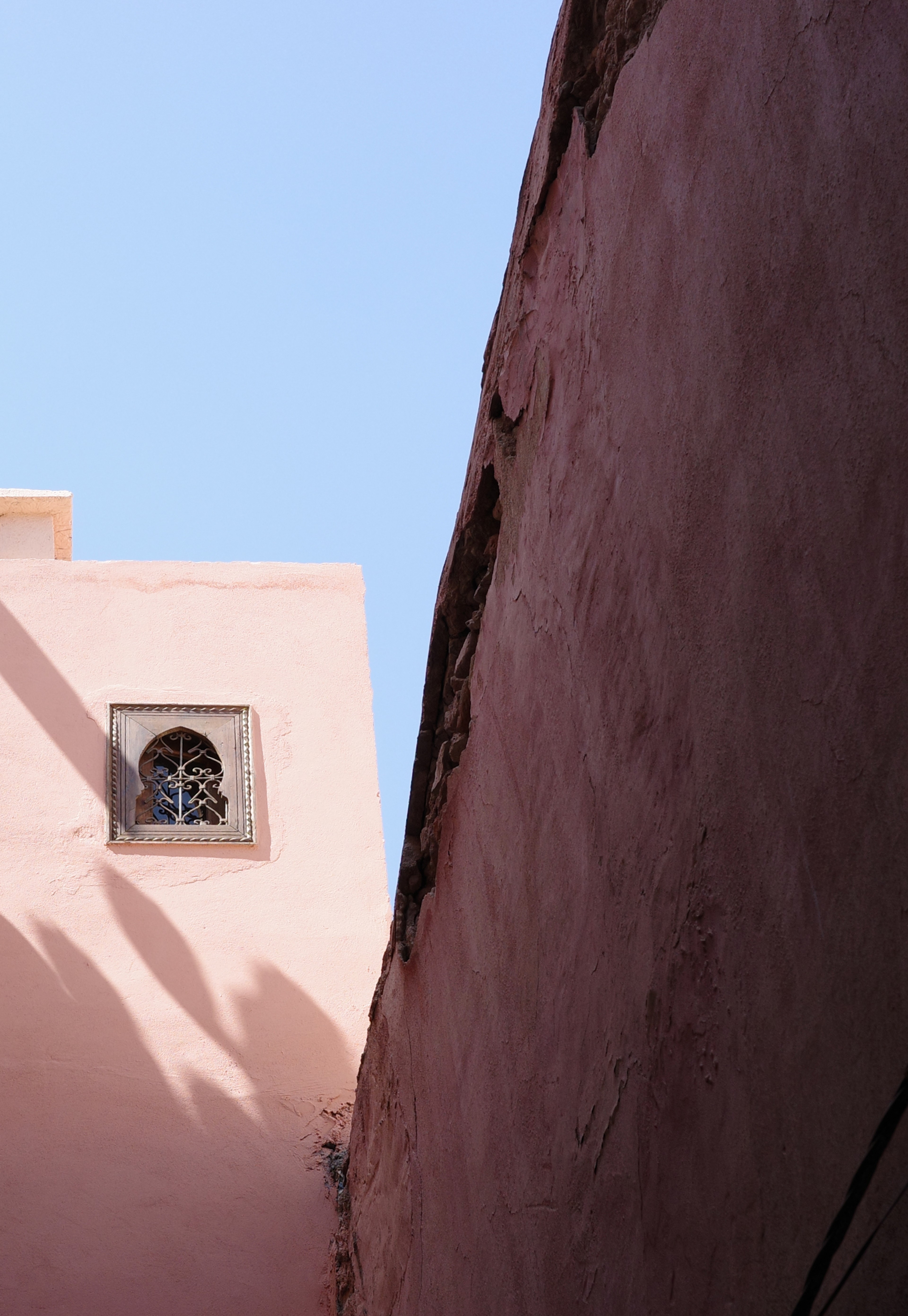 A narrow gap between tall pink walls opens onto a pale blue sky.