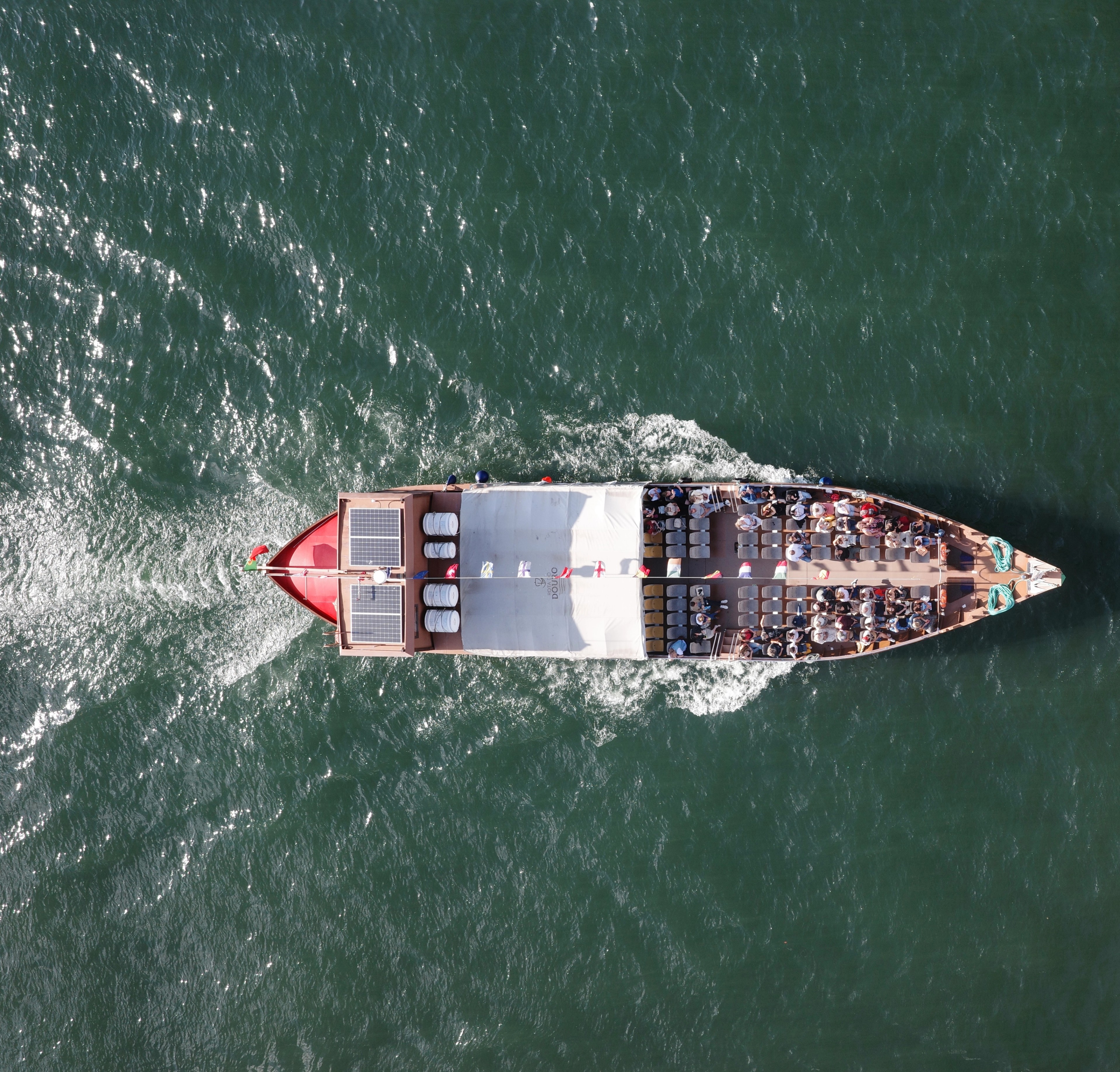An overhead view of a long boat crossing green river water.