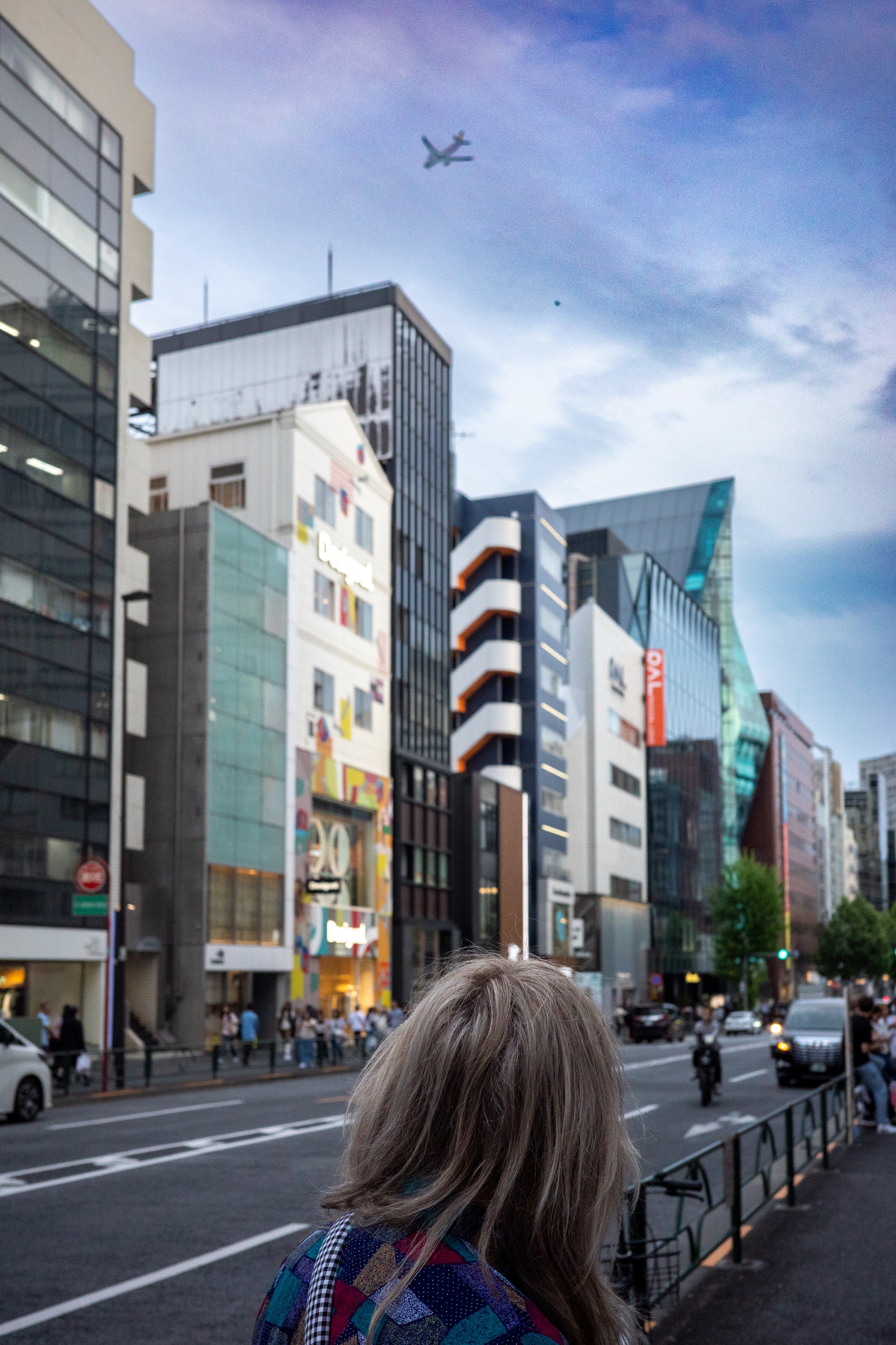 A woman walks along a city street between tall buildings.