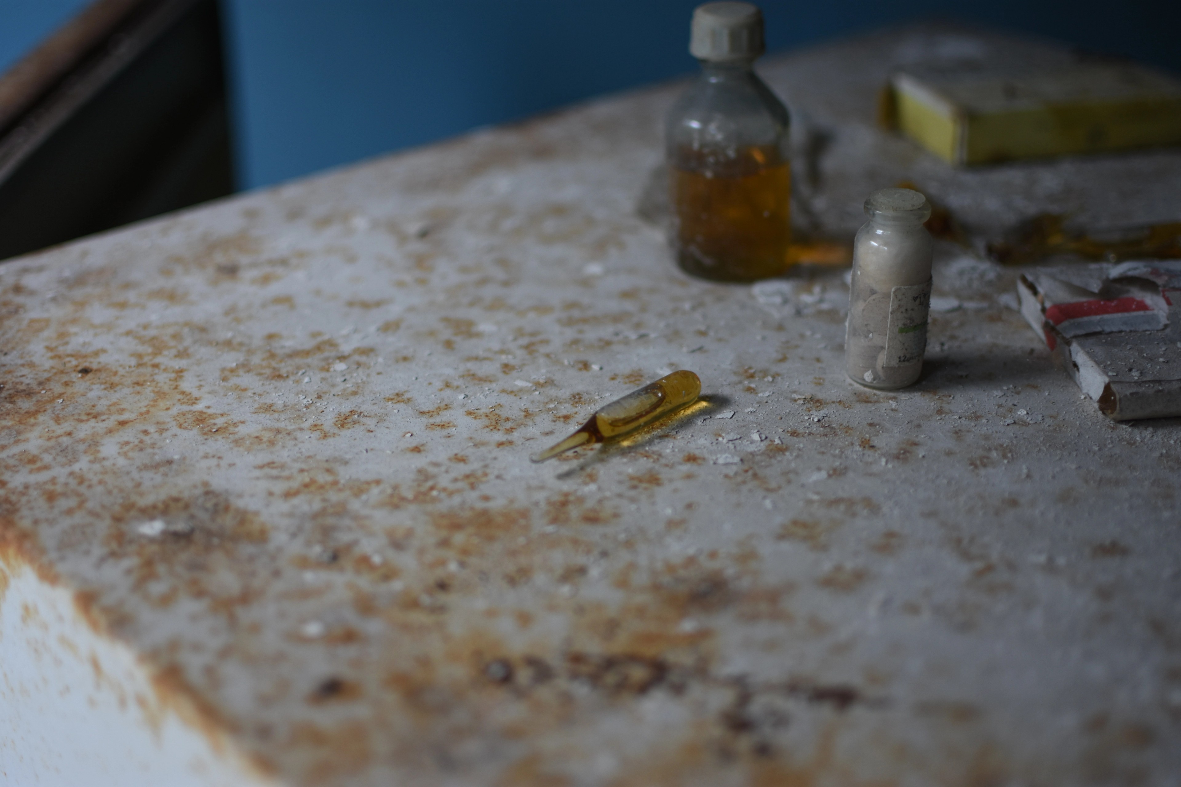 A small syringe and bottle sit on a dusty tabletop.