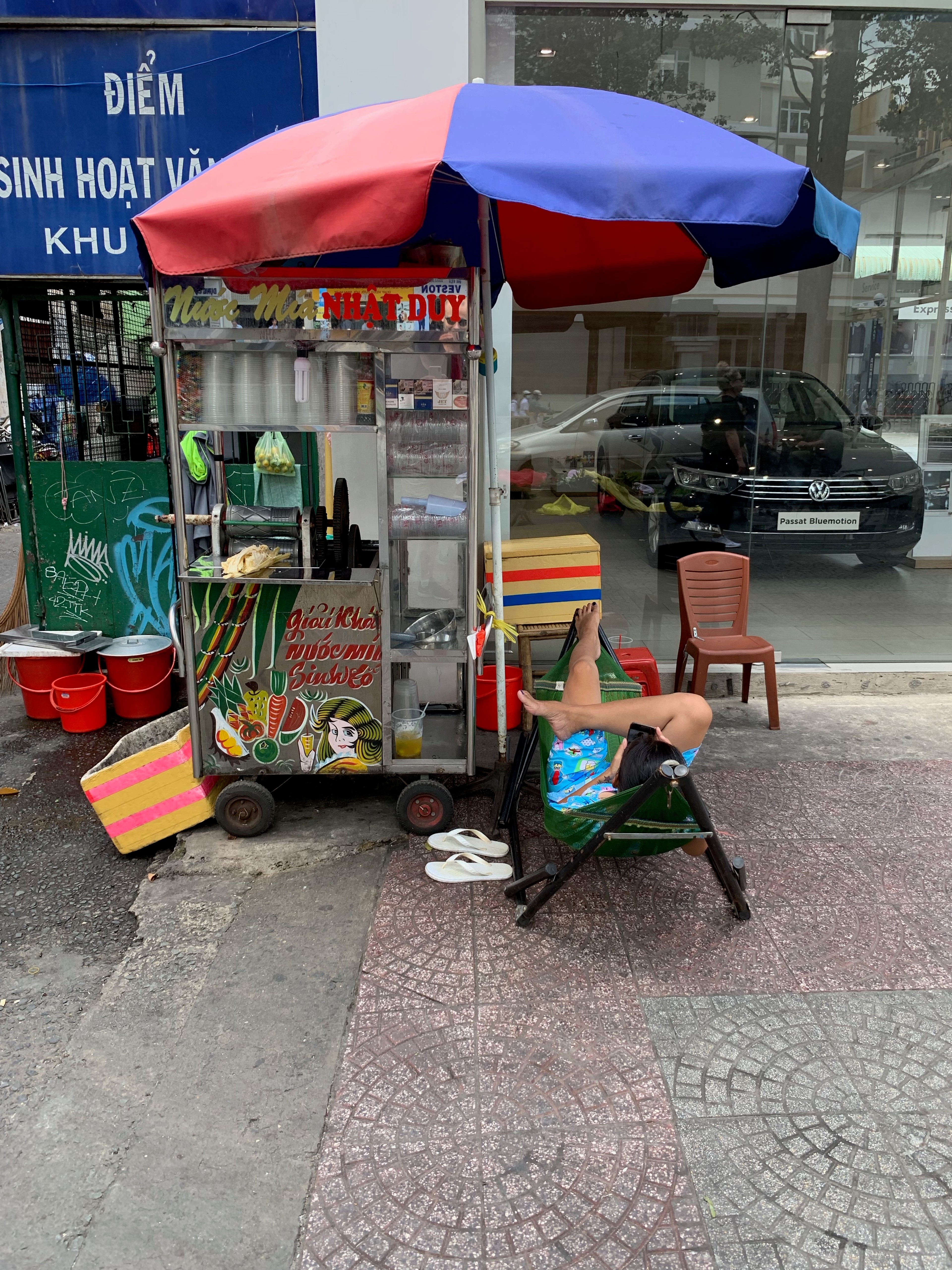 A small street food cart sits beneath a red-and-blue umbrella.