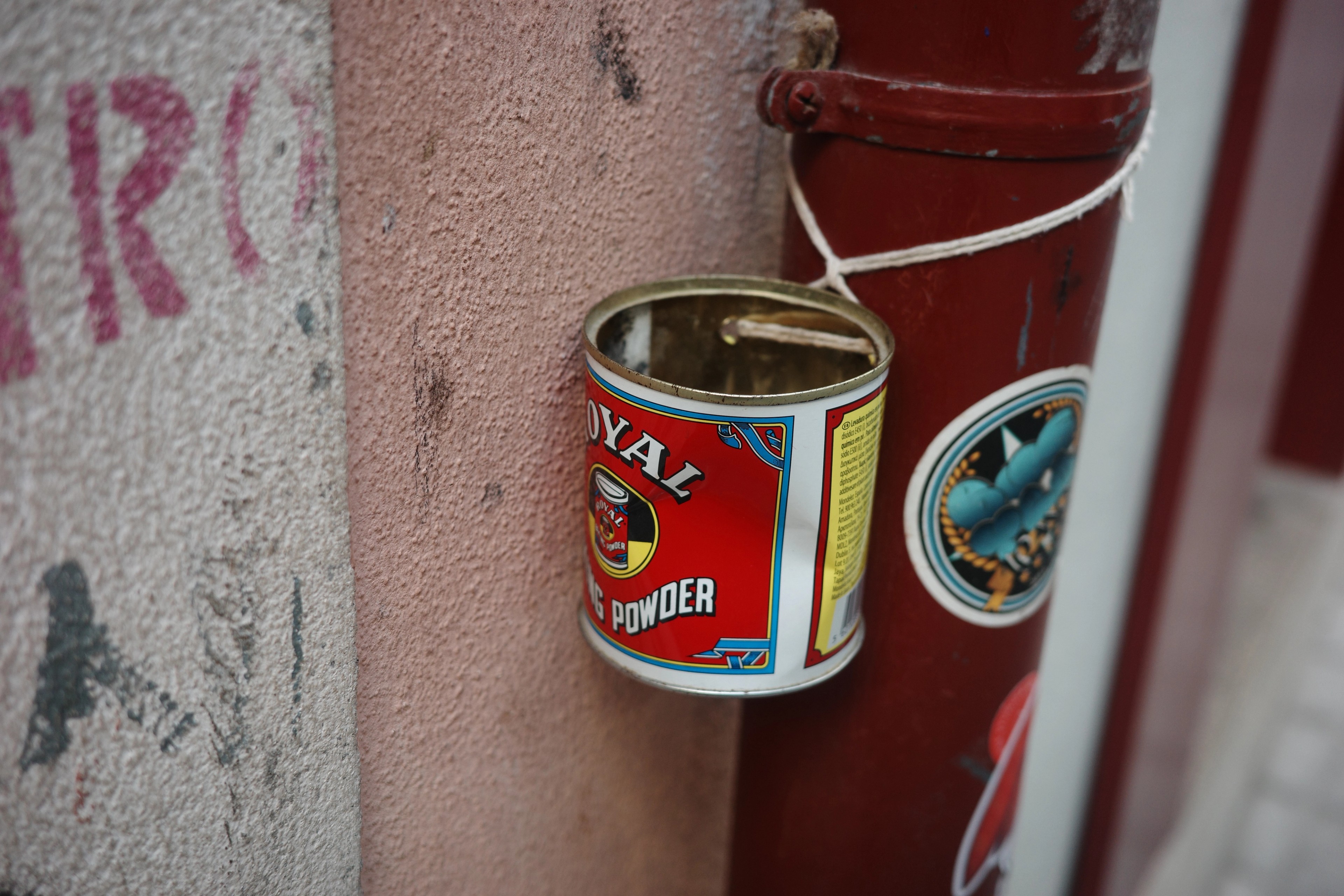 A small tin can hangs by a string against a pink wall marked with graffiti.