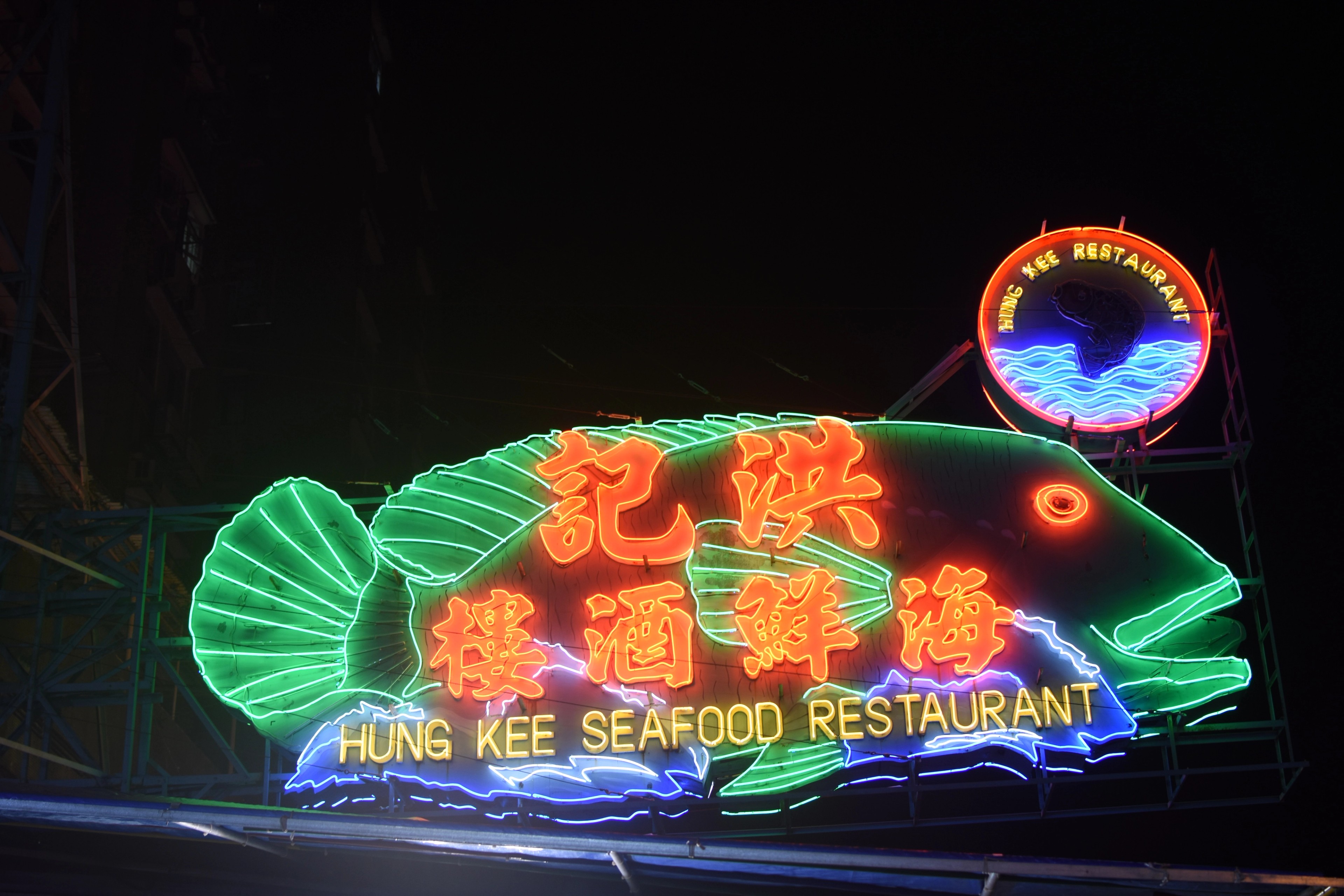 A green neon fish sign advertises a seafood restaurant at night.