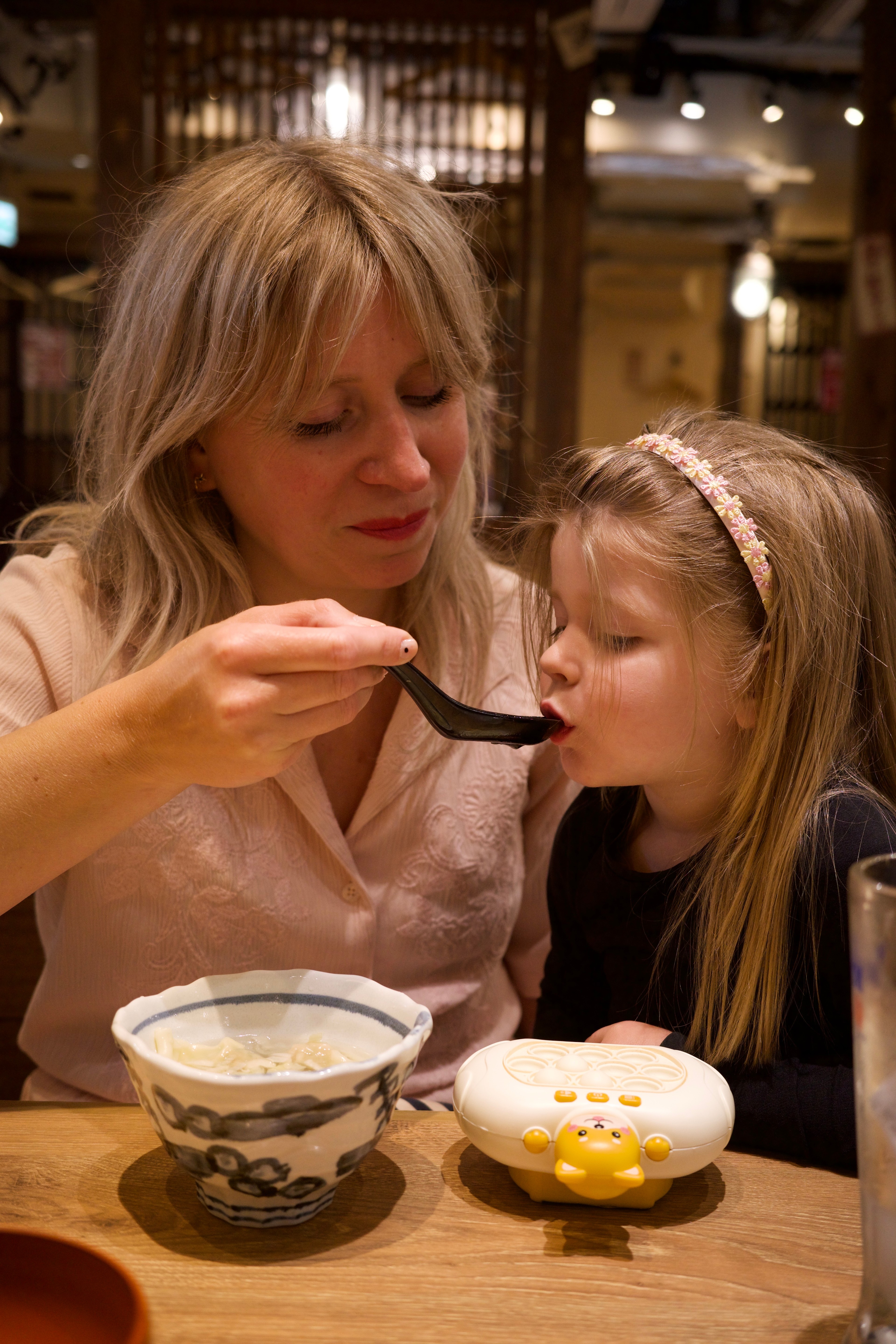 A woman feeds a young child at a restaurant table.