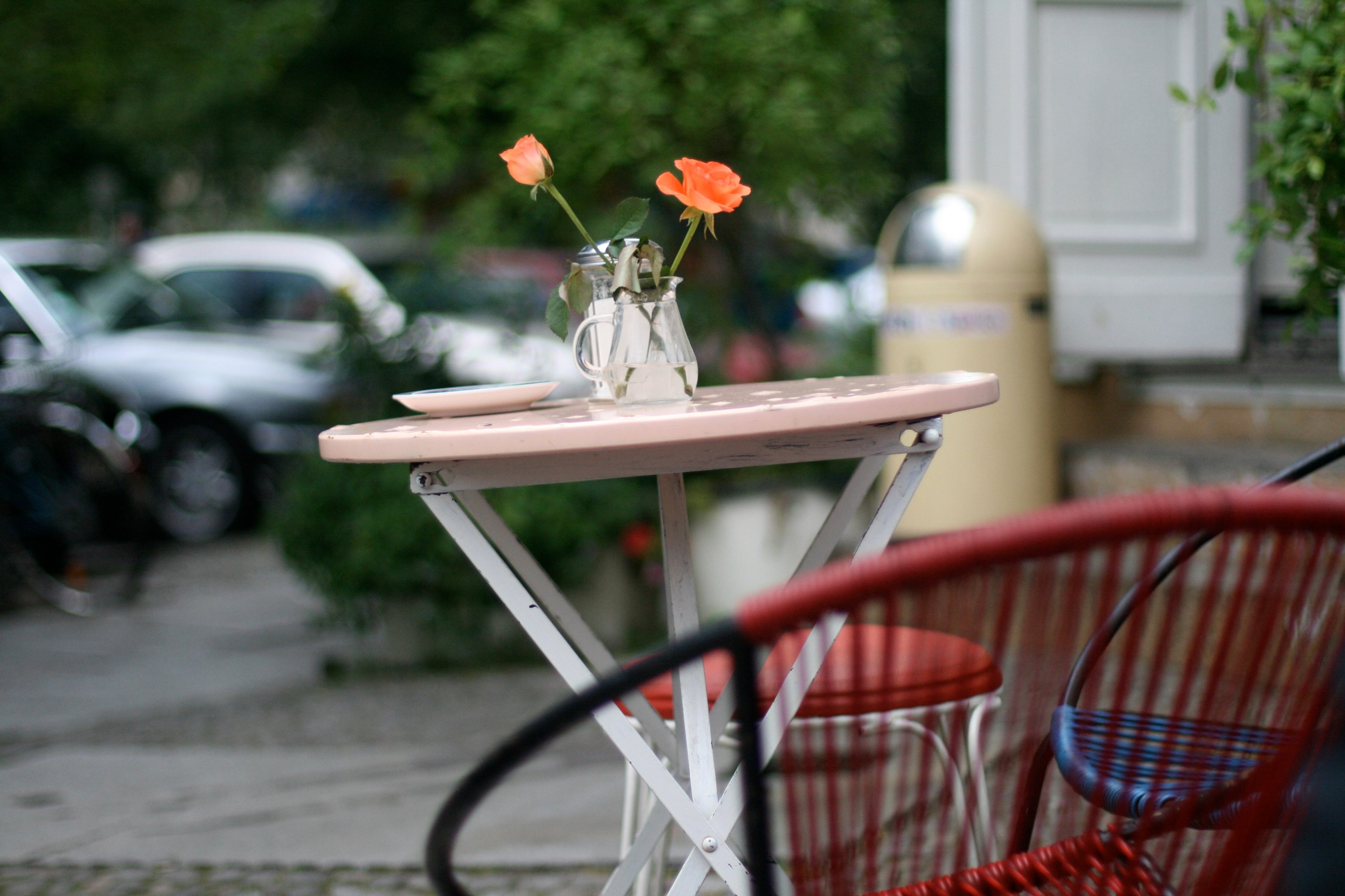 A small vase of flowers sits on a café table beside red chairs.