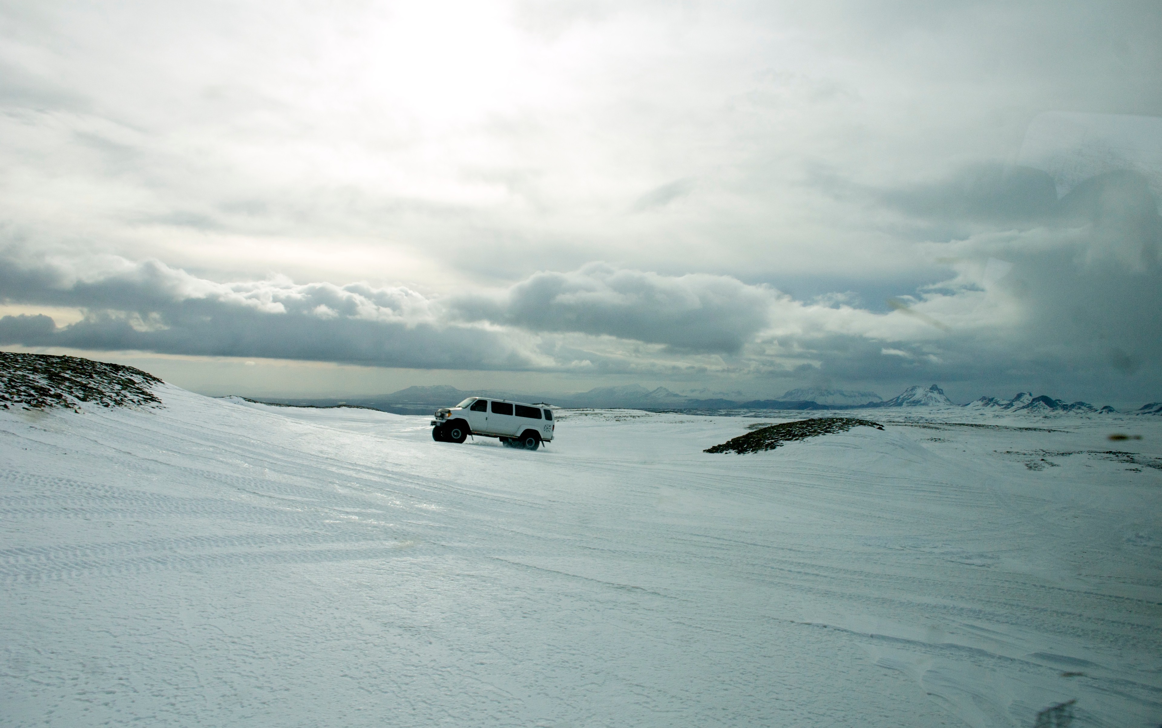 A white vehicle is parked on a broad snowfield under a cloudy sky.