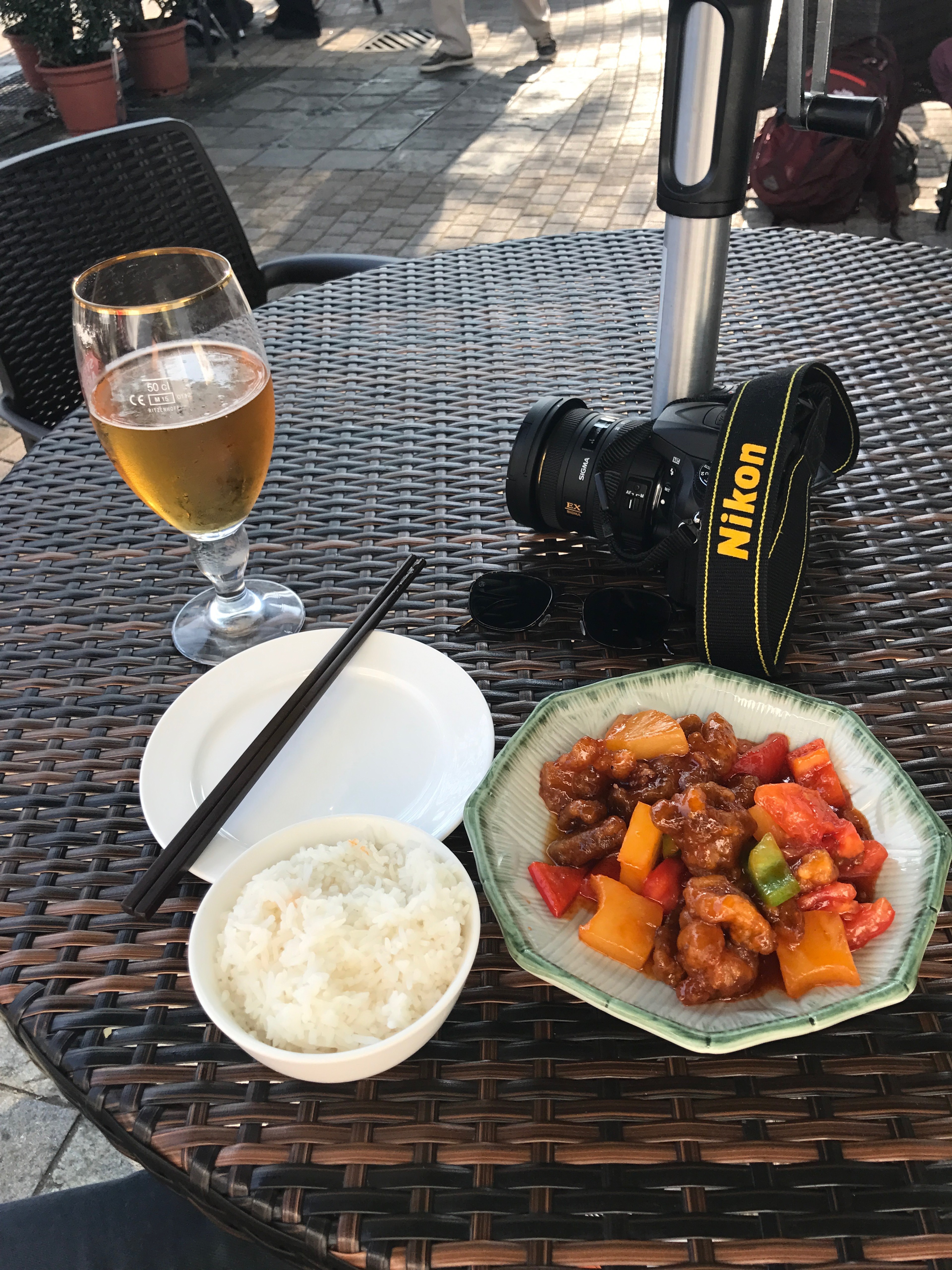 Rice and meat sit beside a camera and drink on an outdoor café table.