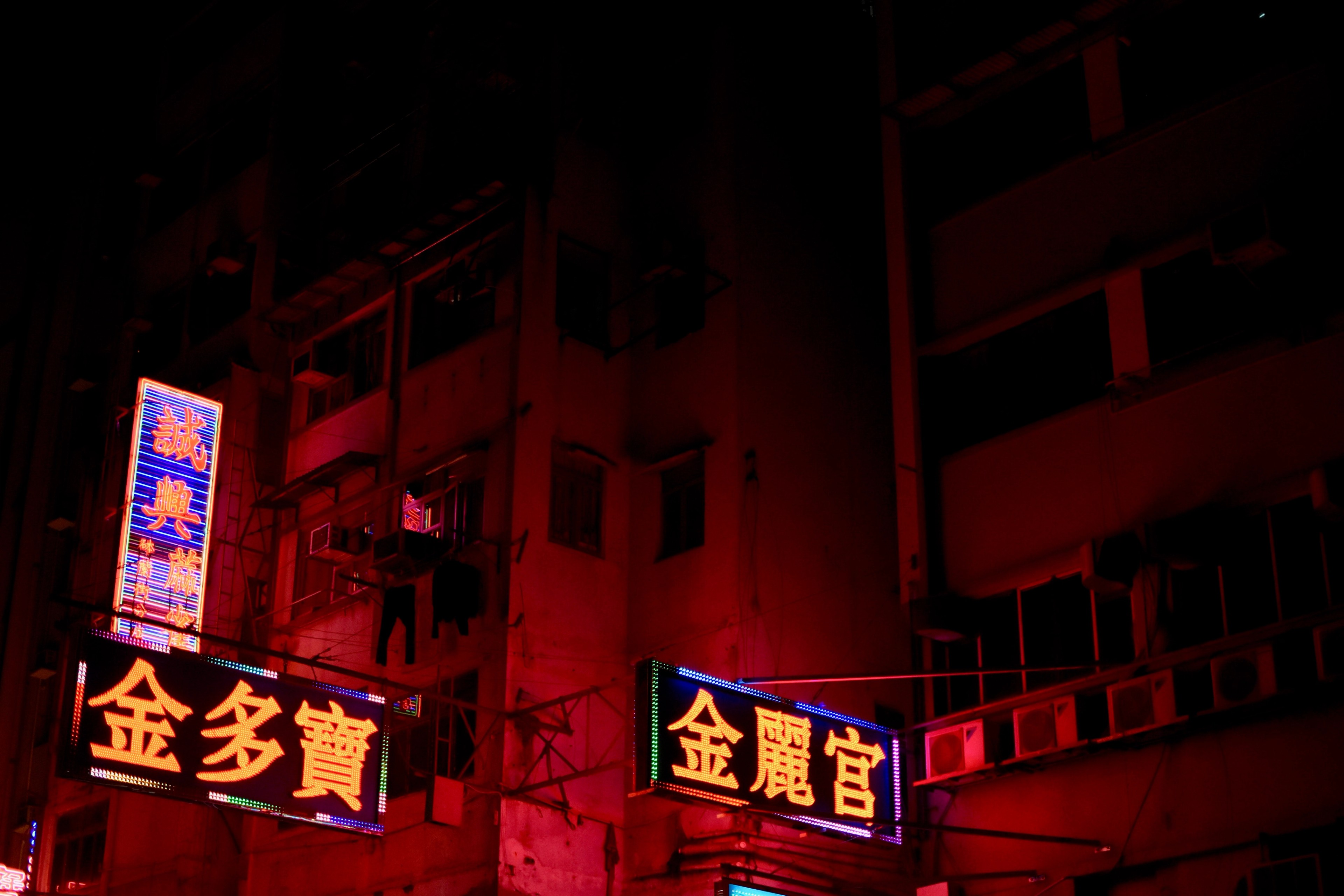Red Chinese-language neon signs glow beneath dark apartment windows.