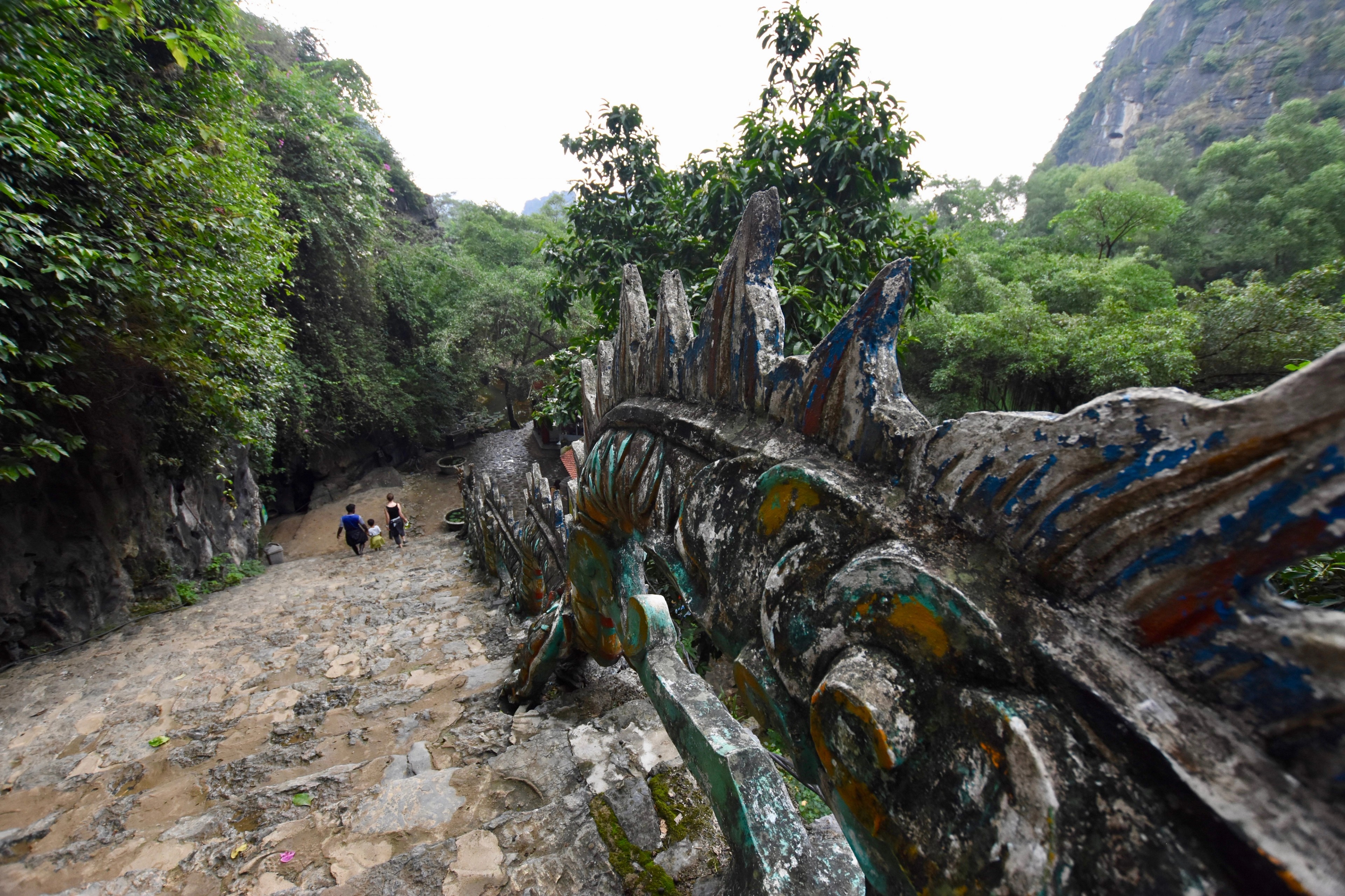 A carved stone walkway with sculpted railings follows a green mountainside.