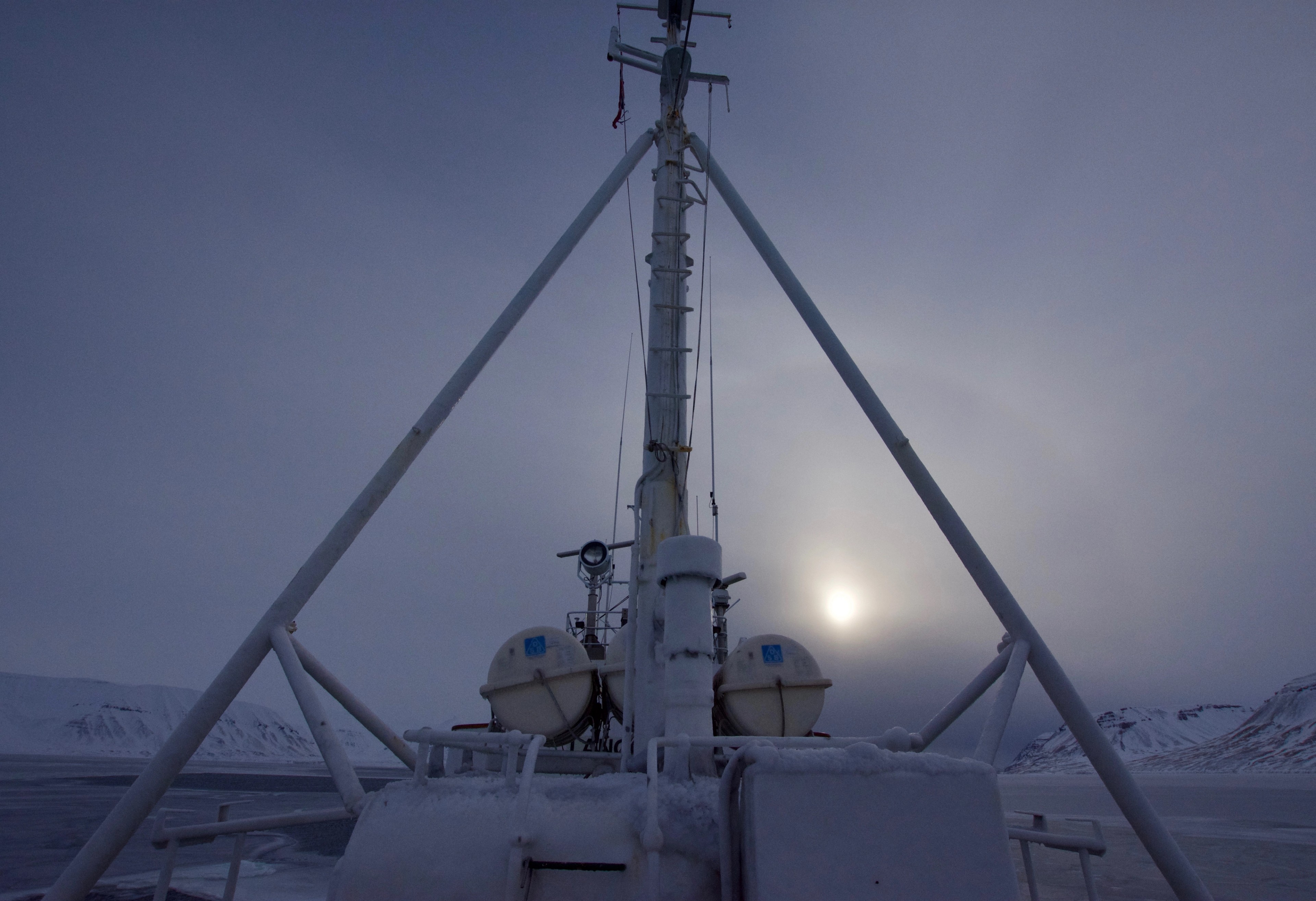 A mast rises above a boat deck against an overcast sky.
