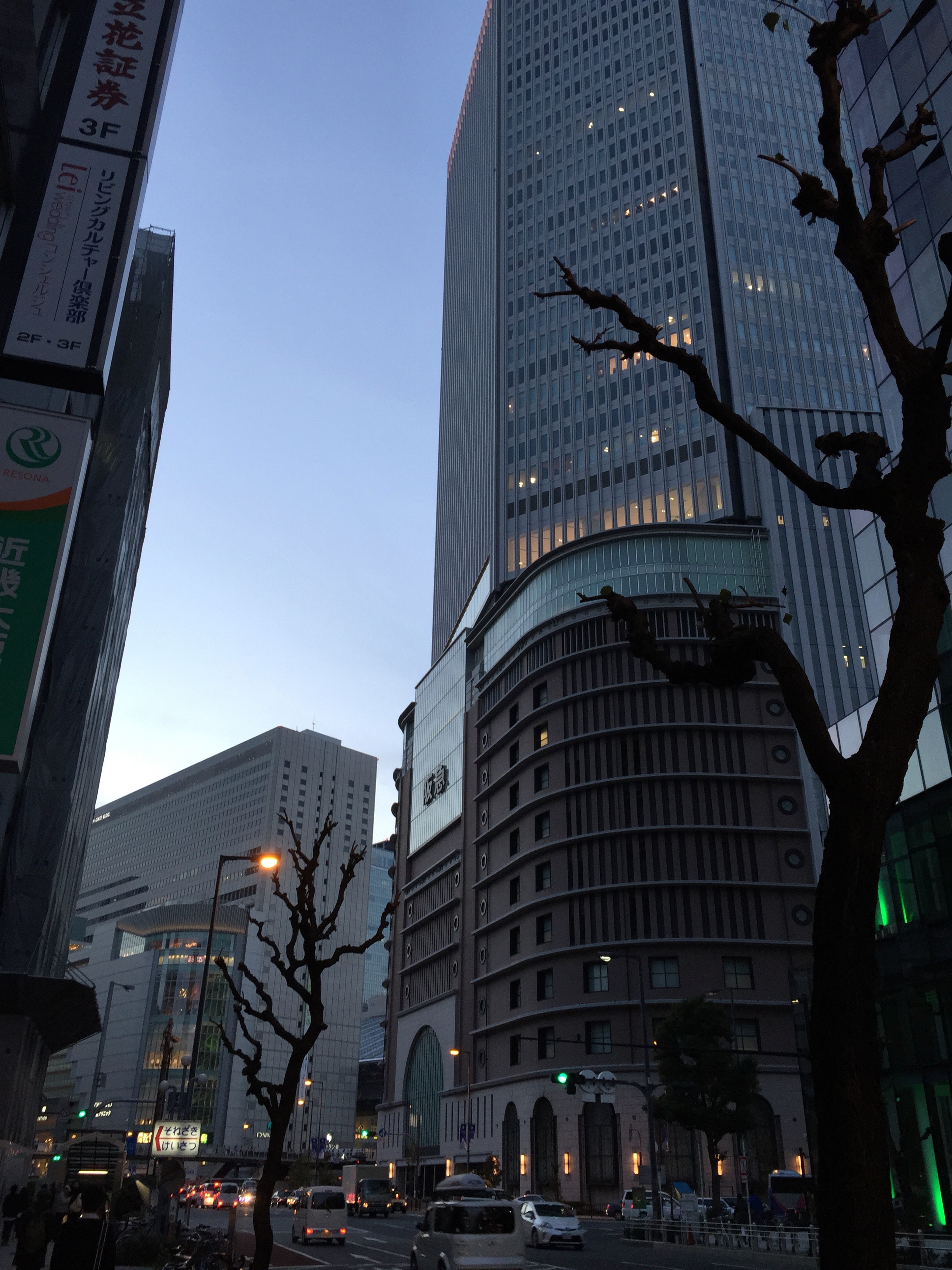 A glass office tower rises above the city at dusk.