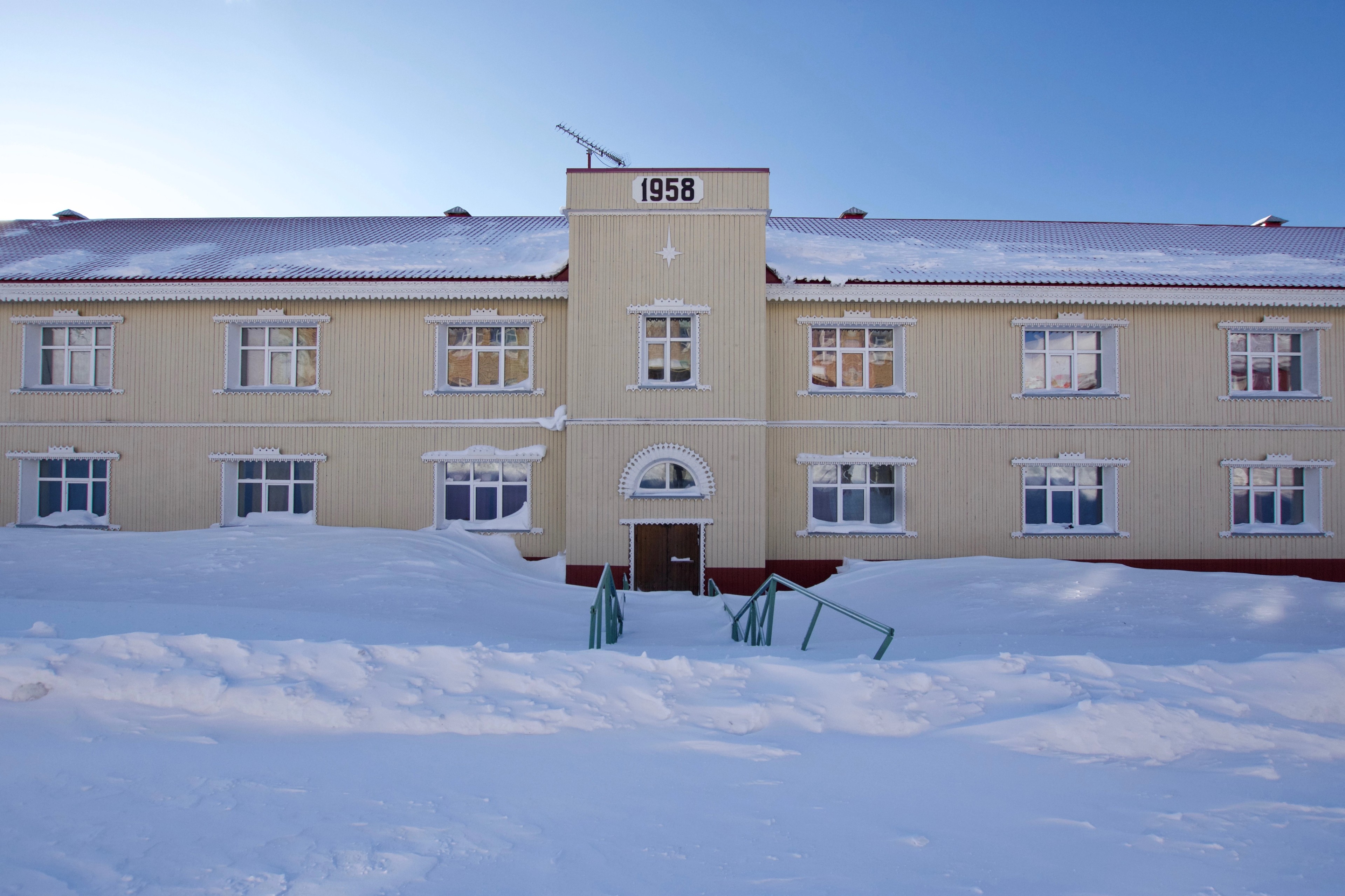 A pale building with a central entrance stands in the snow.