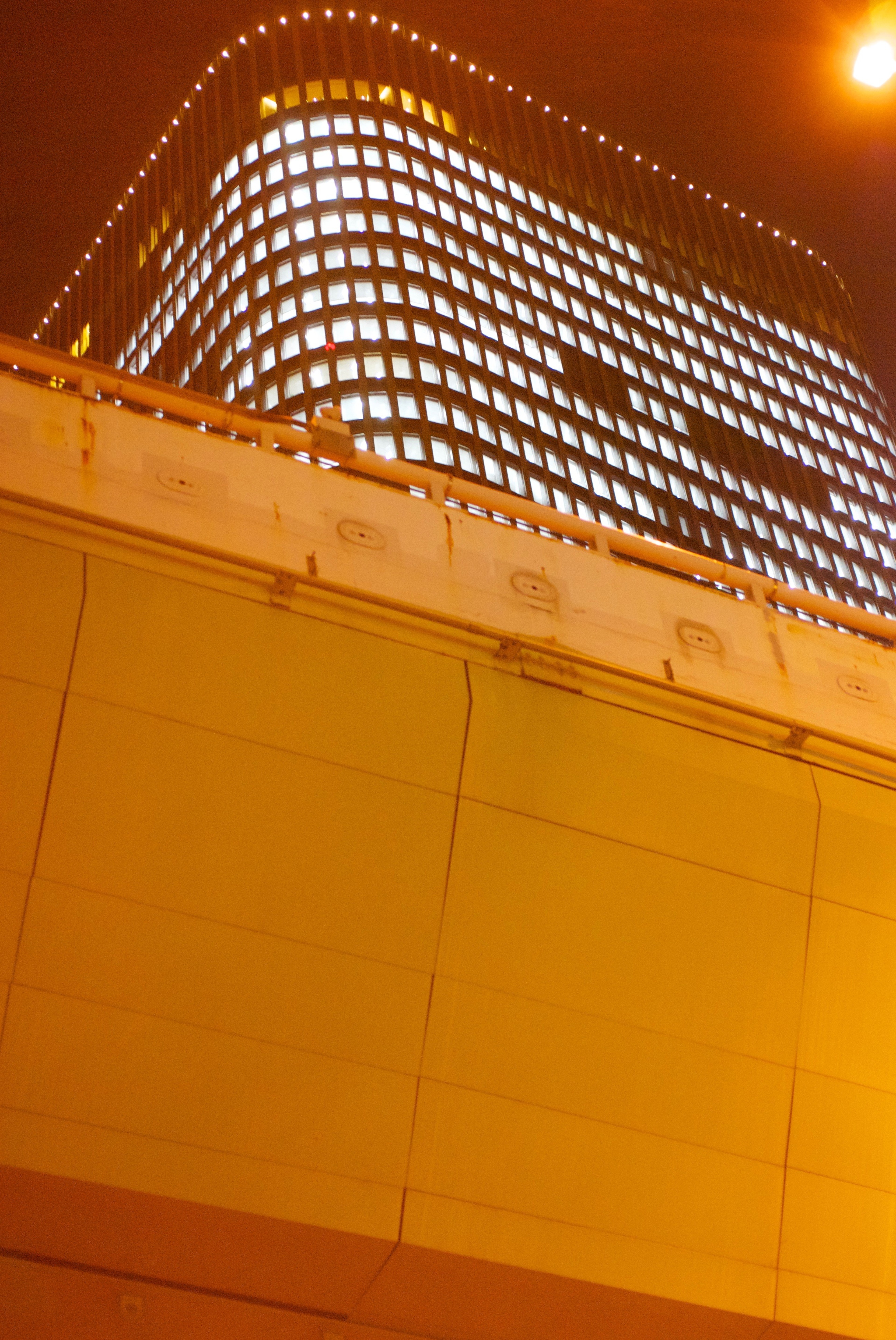 A modern building is partly obscured by warm orange lights at night.