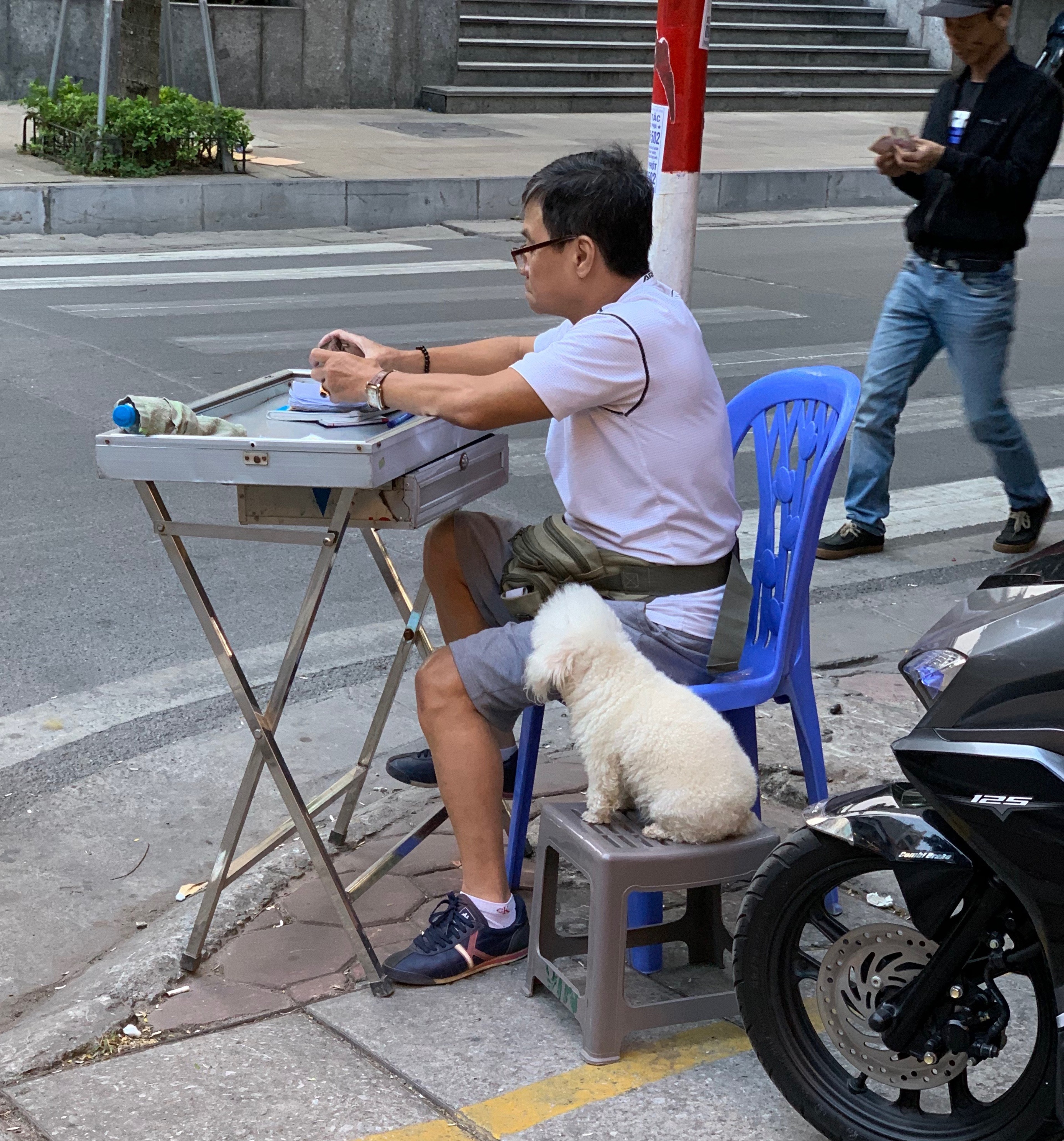 A man sits beside an outdoor cooking cart on the sidewalk.