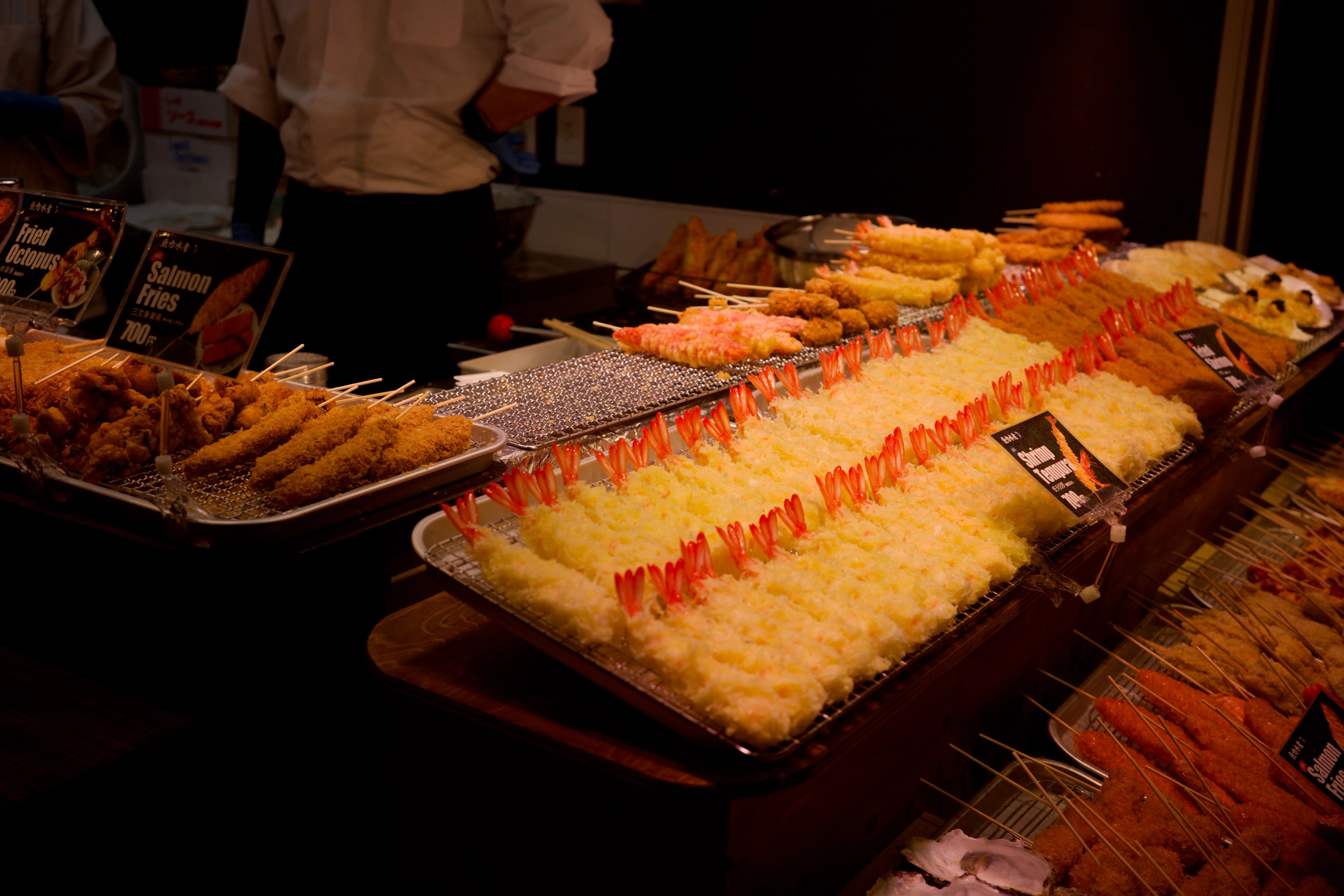 Golden fried snacks fill trays in a market stall.