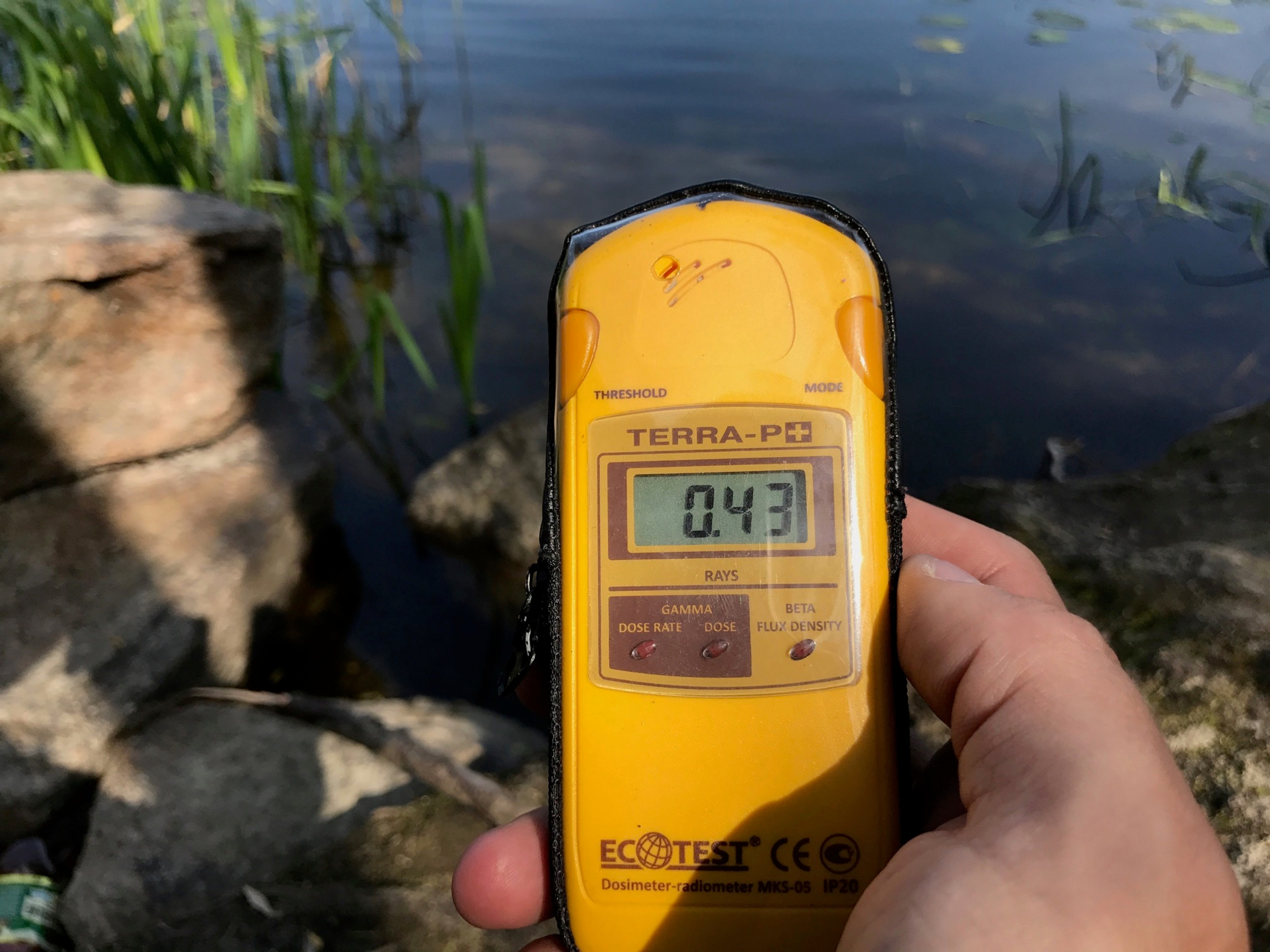 A handheld yellow radiation meter reads 0.43 near the ground.