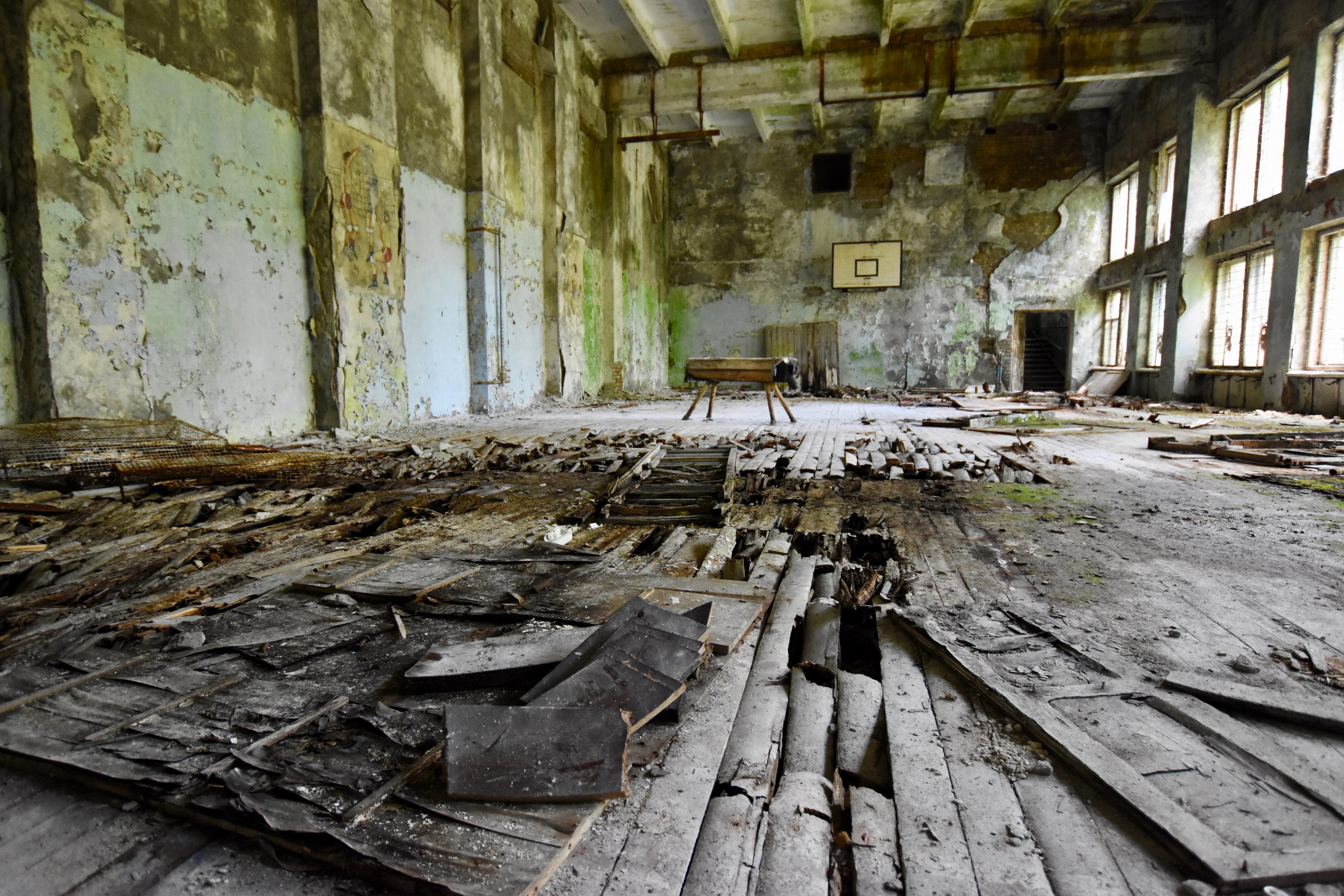 An abandoned hall with broken flooring and daylight through windows.