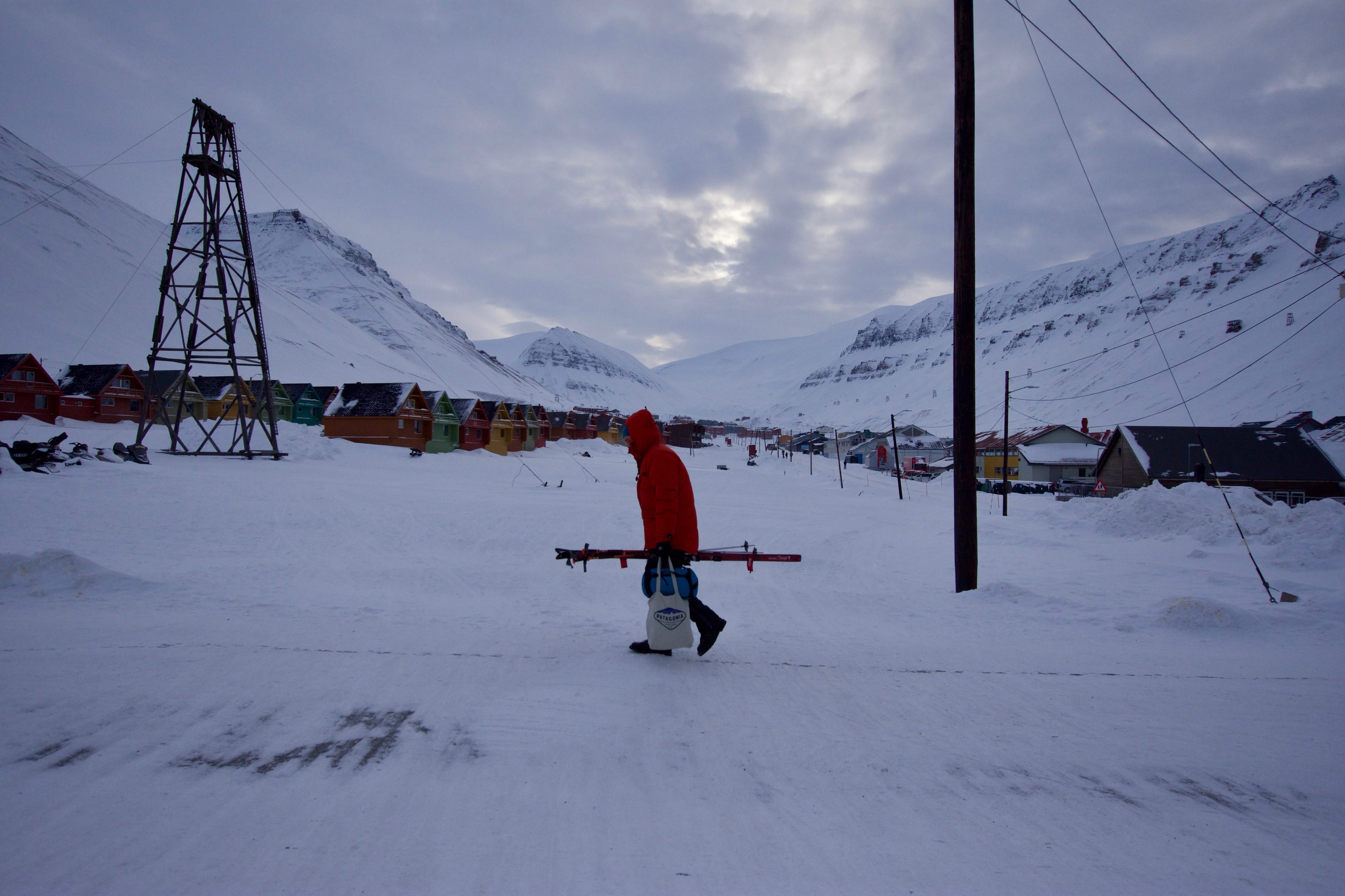 A person crosses a snowy street beside utility poles and houses.