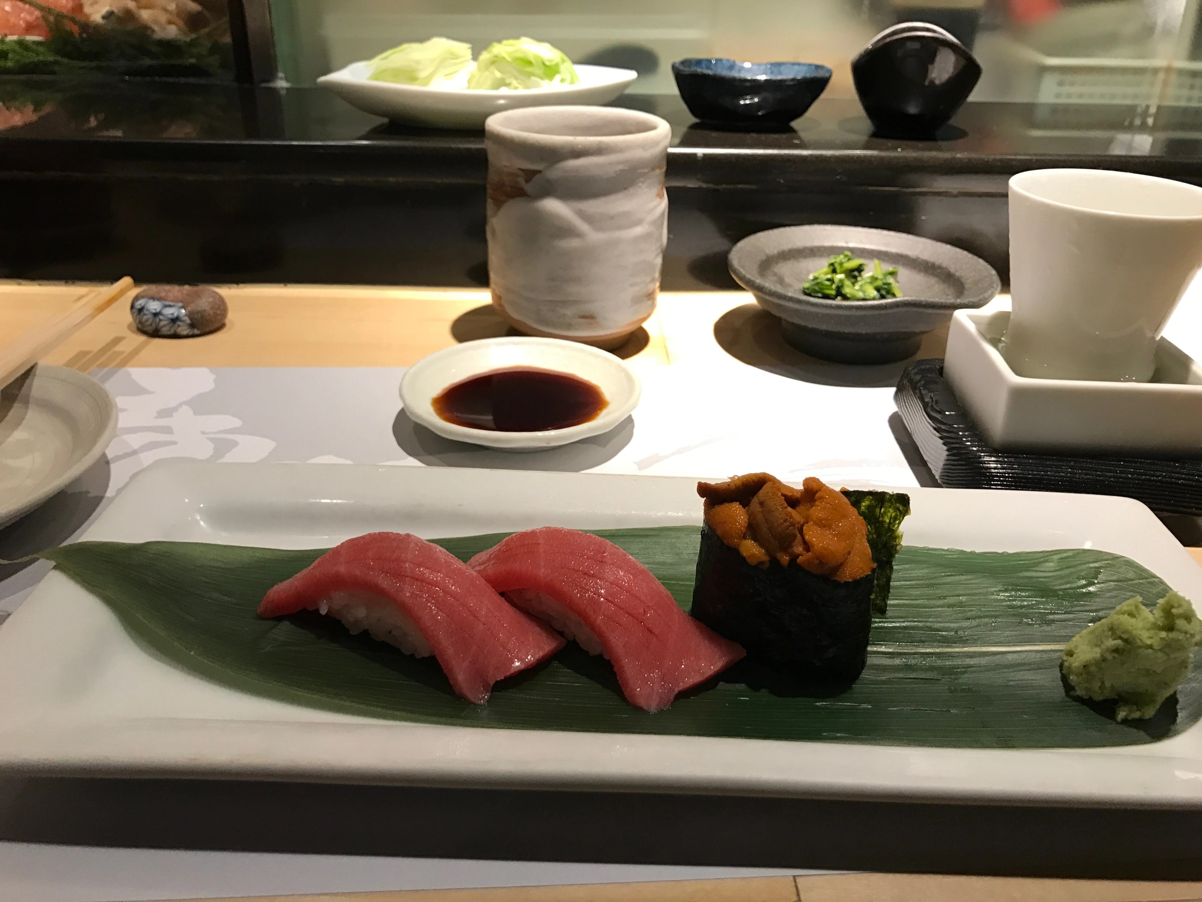 A selection of sushi is arranged in a black tray with tea cups nearby.