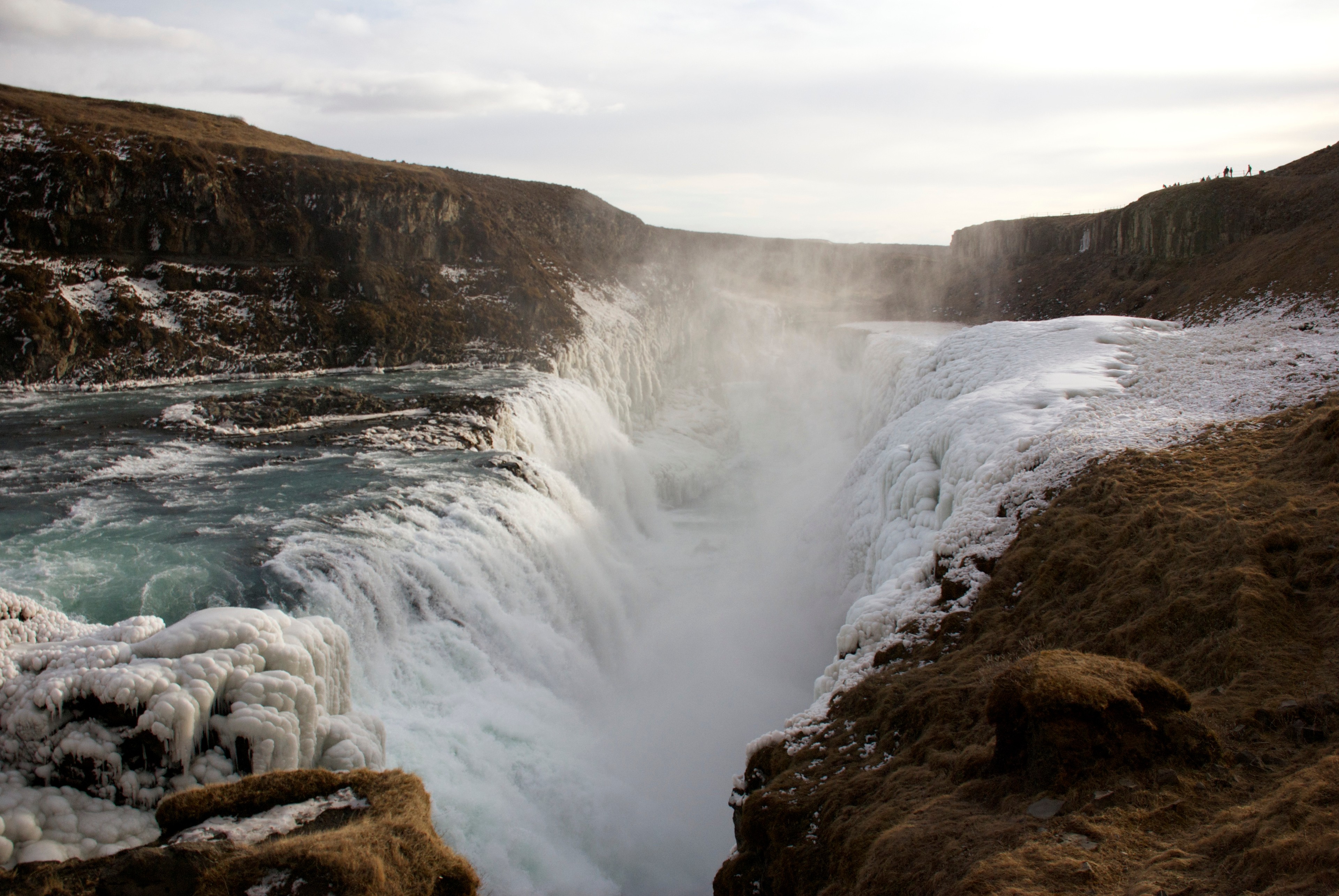 A broad waterfall pours over a dark rock ledge into a foaming river.
