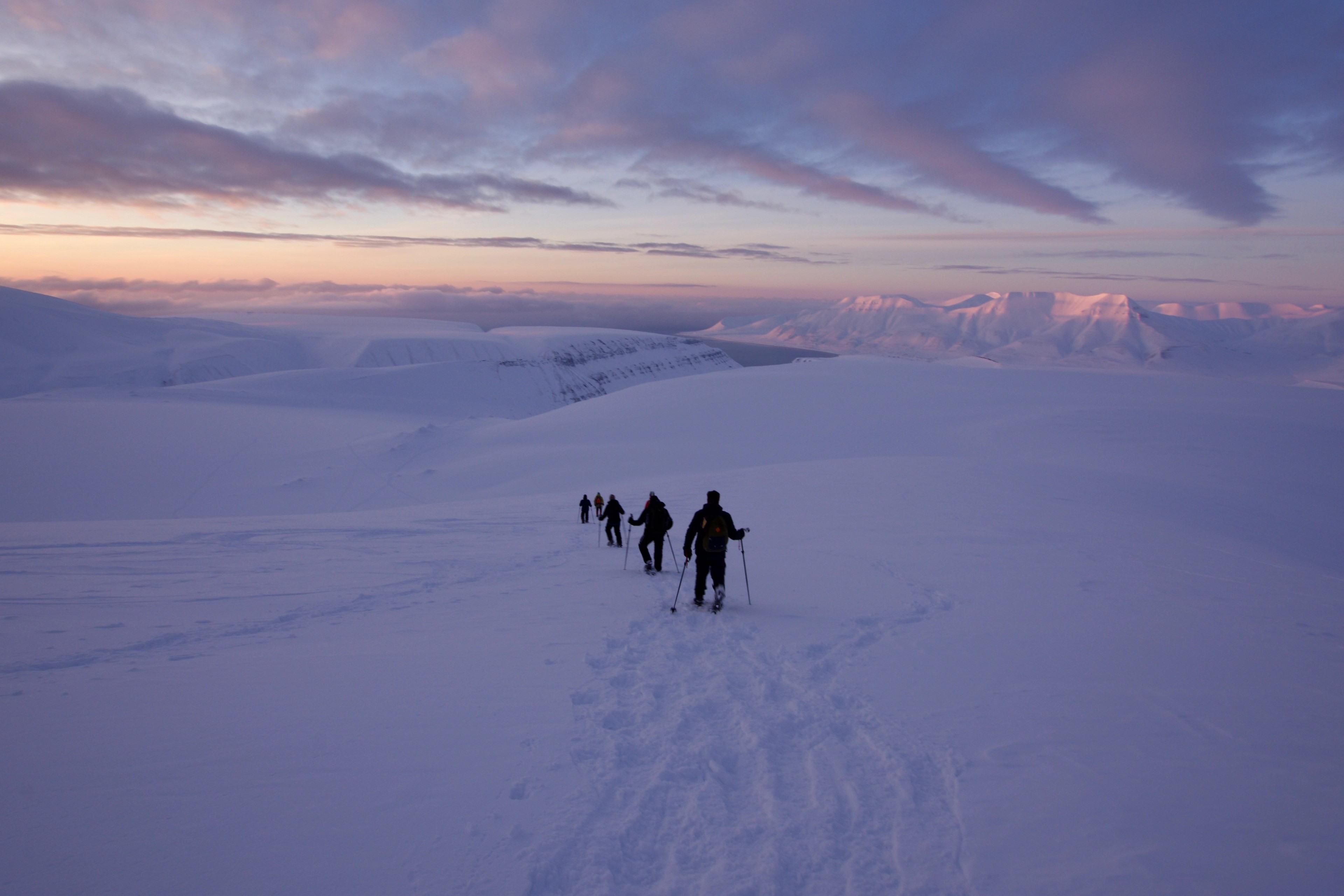 Hikers walk across a snowfield at sunset.