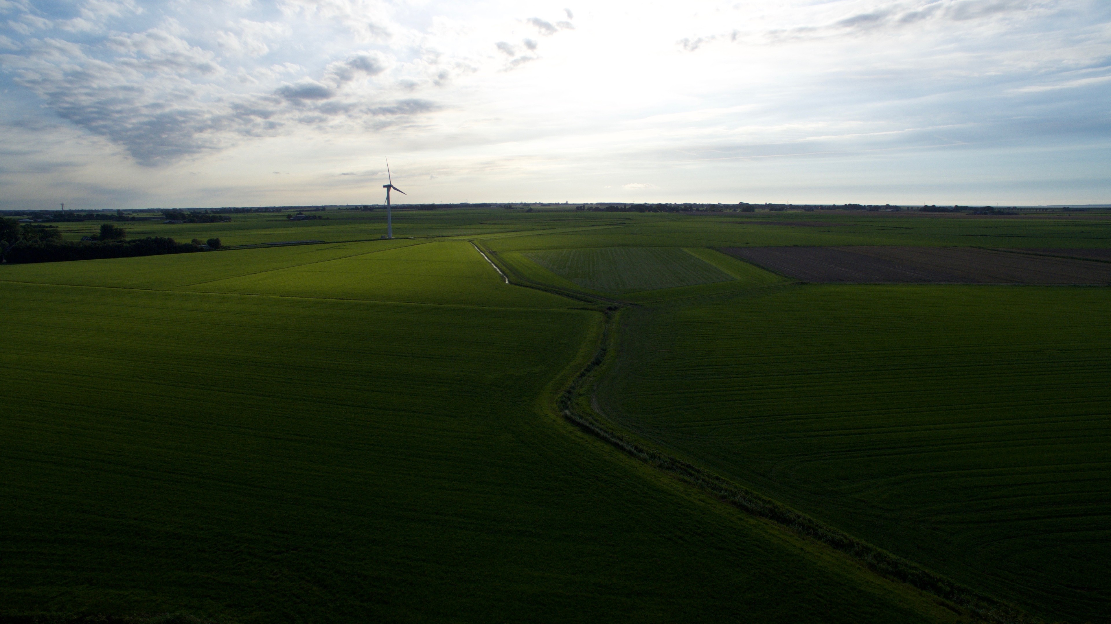 Aerial view across broad green fields beneath a cloudy sky.