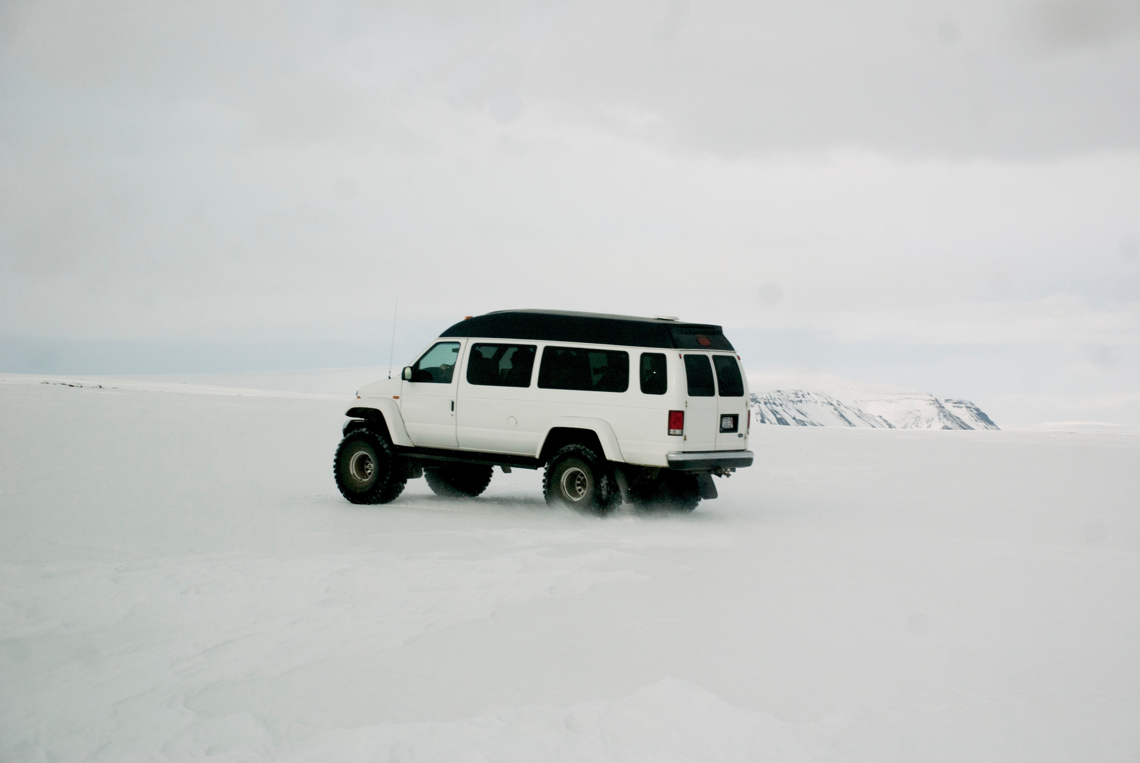 A white four-wheel-drive vehicle crosses an open snowfield.