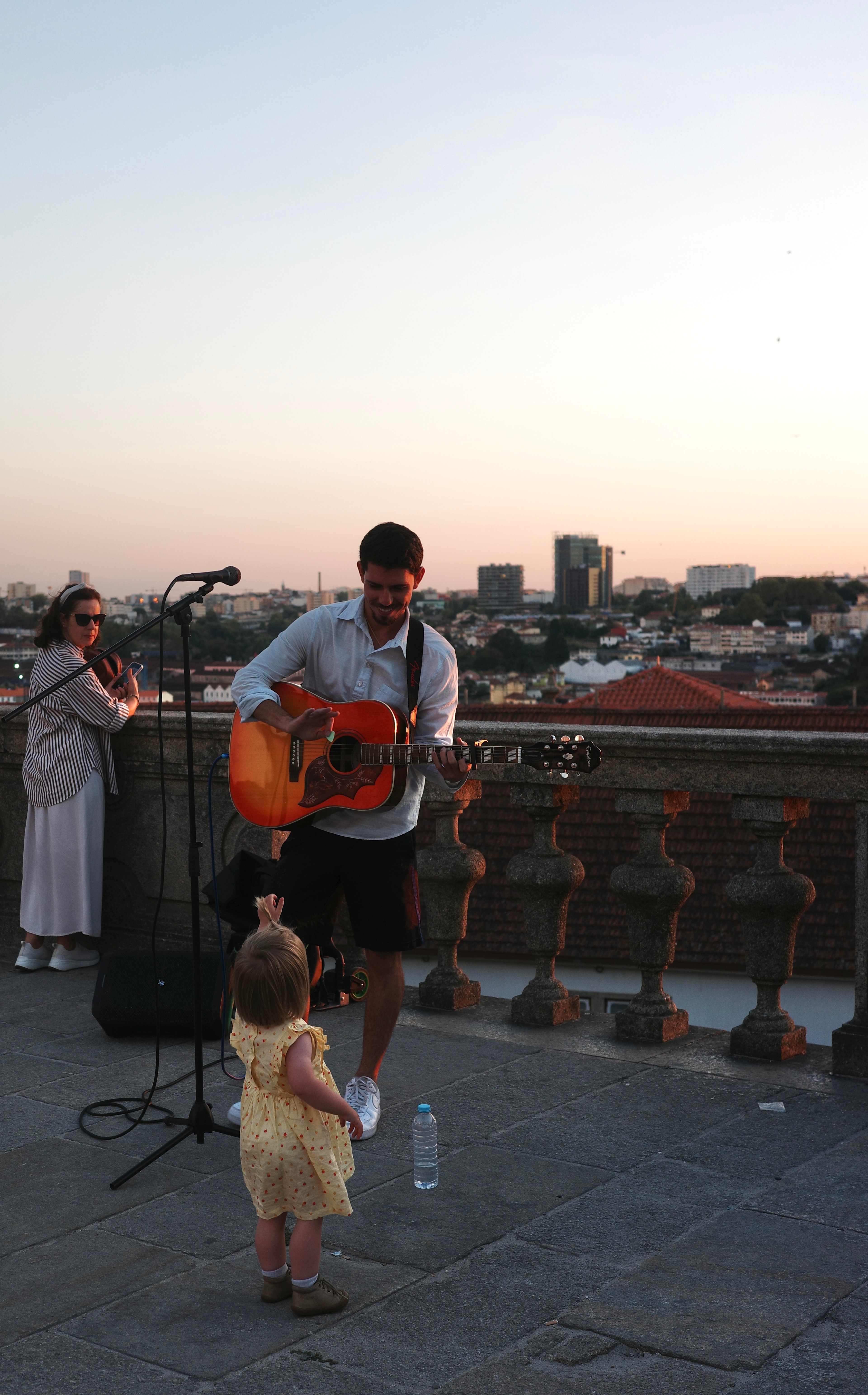 A person and a dog stand by the water at sunset, facing the Porto skyline.