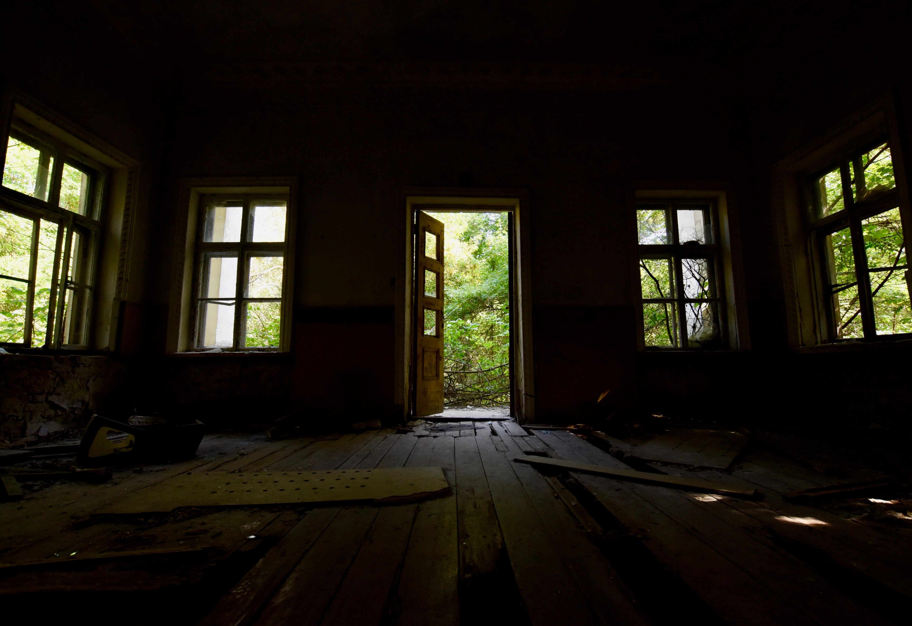 A dark abandoned room with several windows and a doorway.