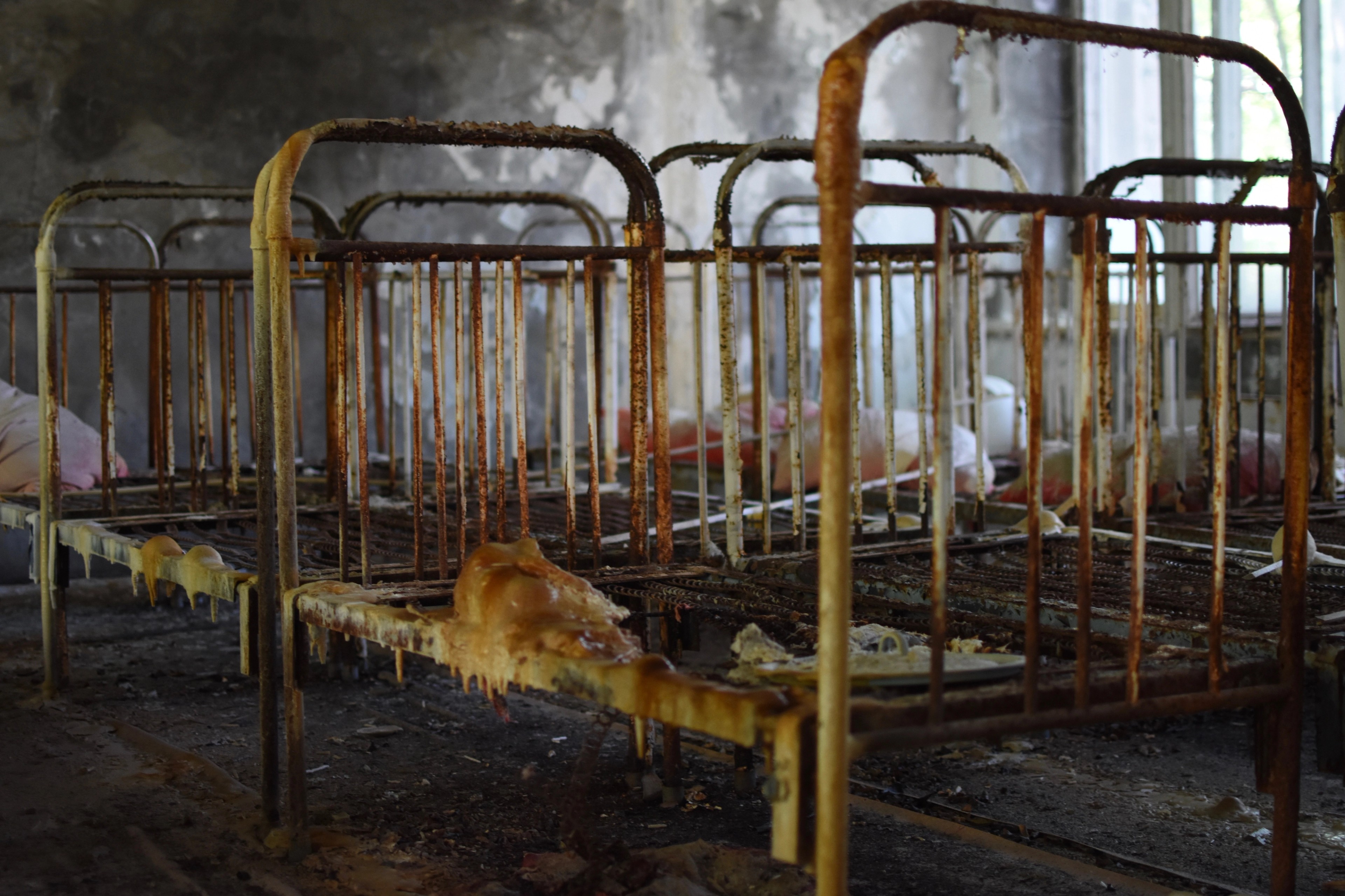 Rusted metal beds stand in an abandoned institutional room.