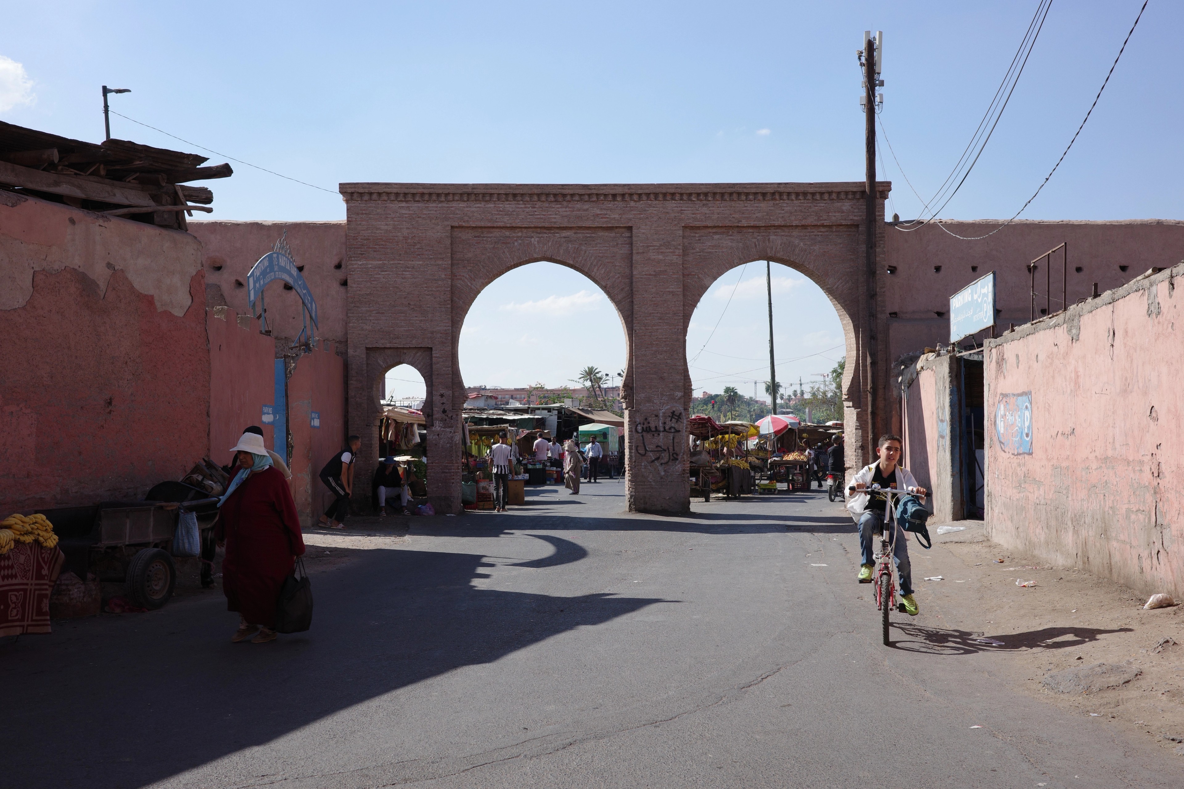 People and bicycles pass through a broad city gate with two large arches.