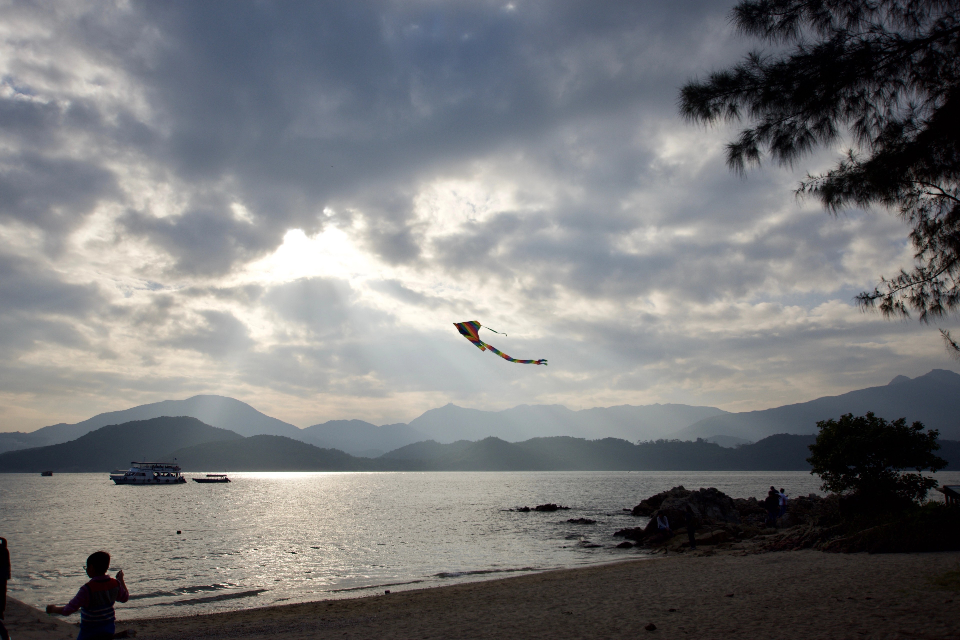 A kite flies over the water and distant islands at sunset.