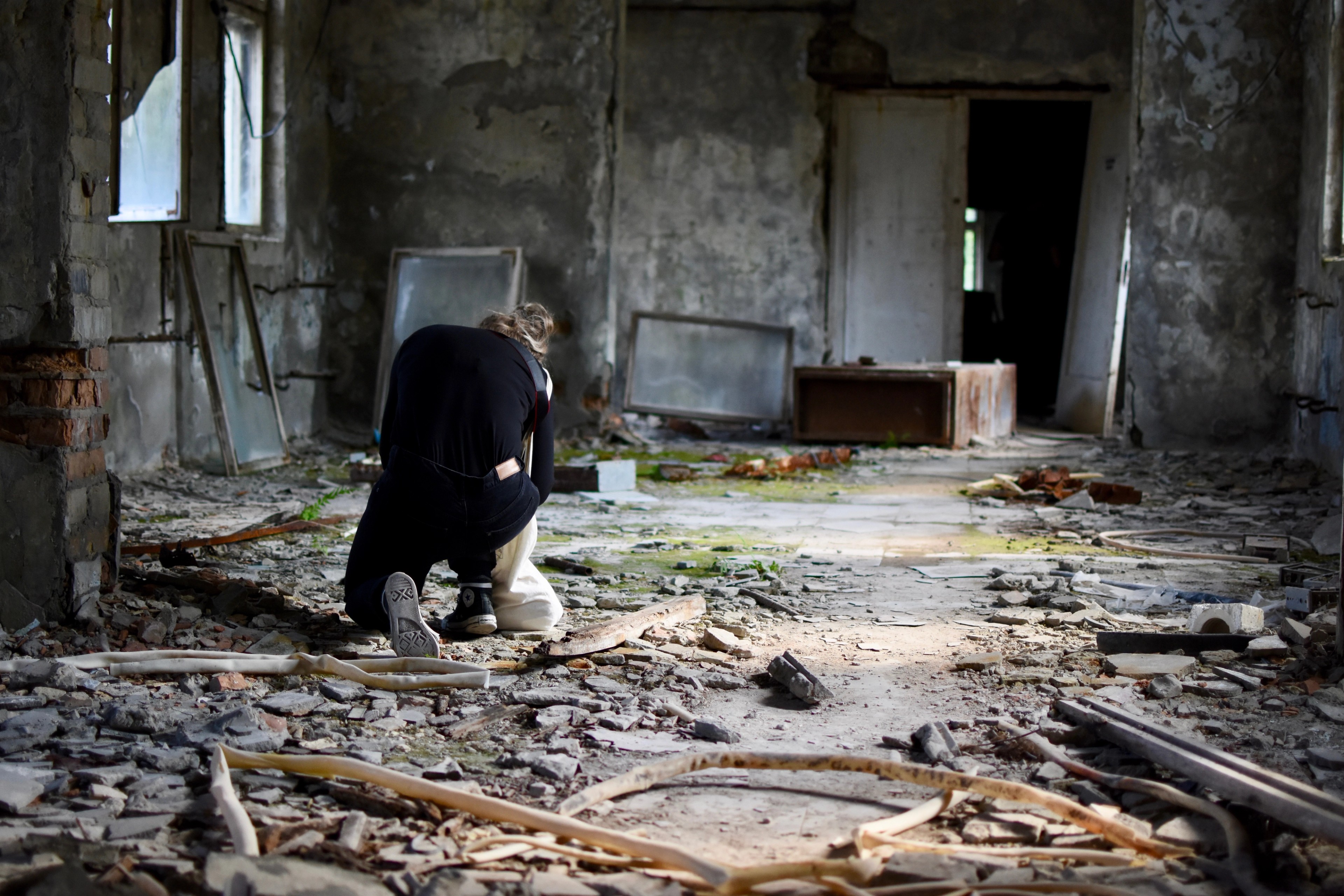 A person kneels among debris in a damaged room.