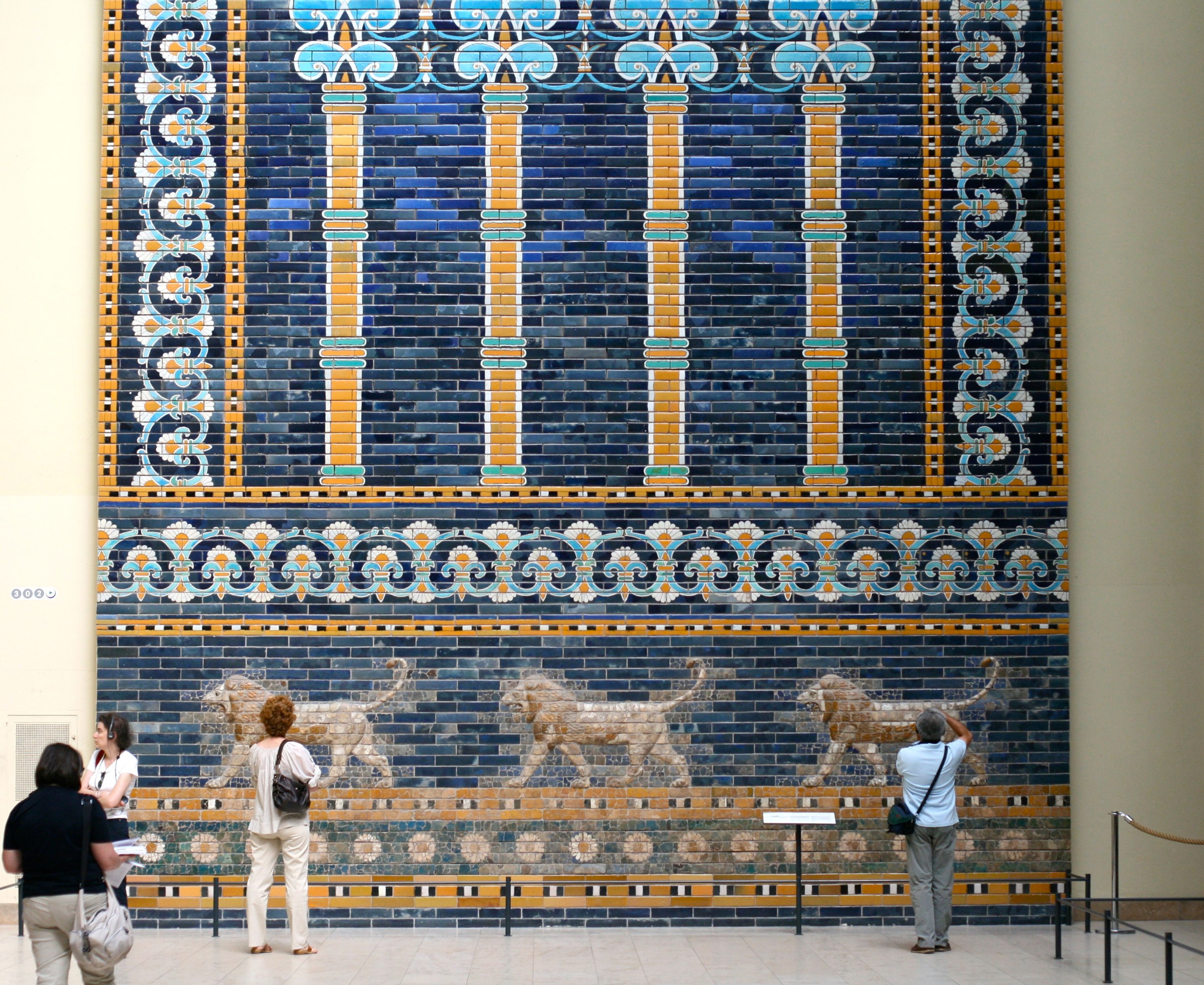 Visitors look at a large blue-and-yellow decorative wall display in a museum.