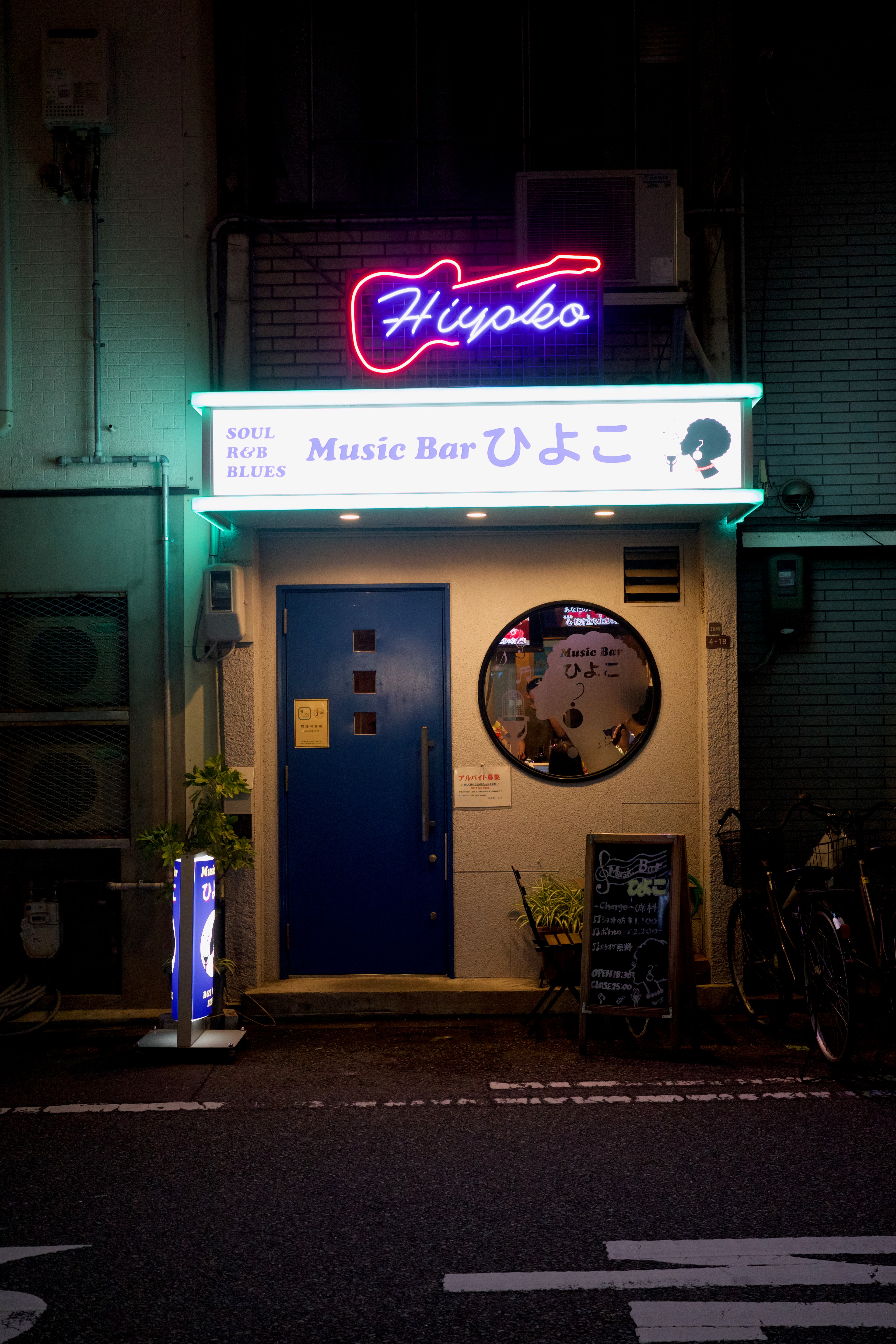 A small storefront glows with colorful signage at night.