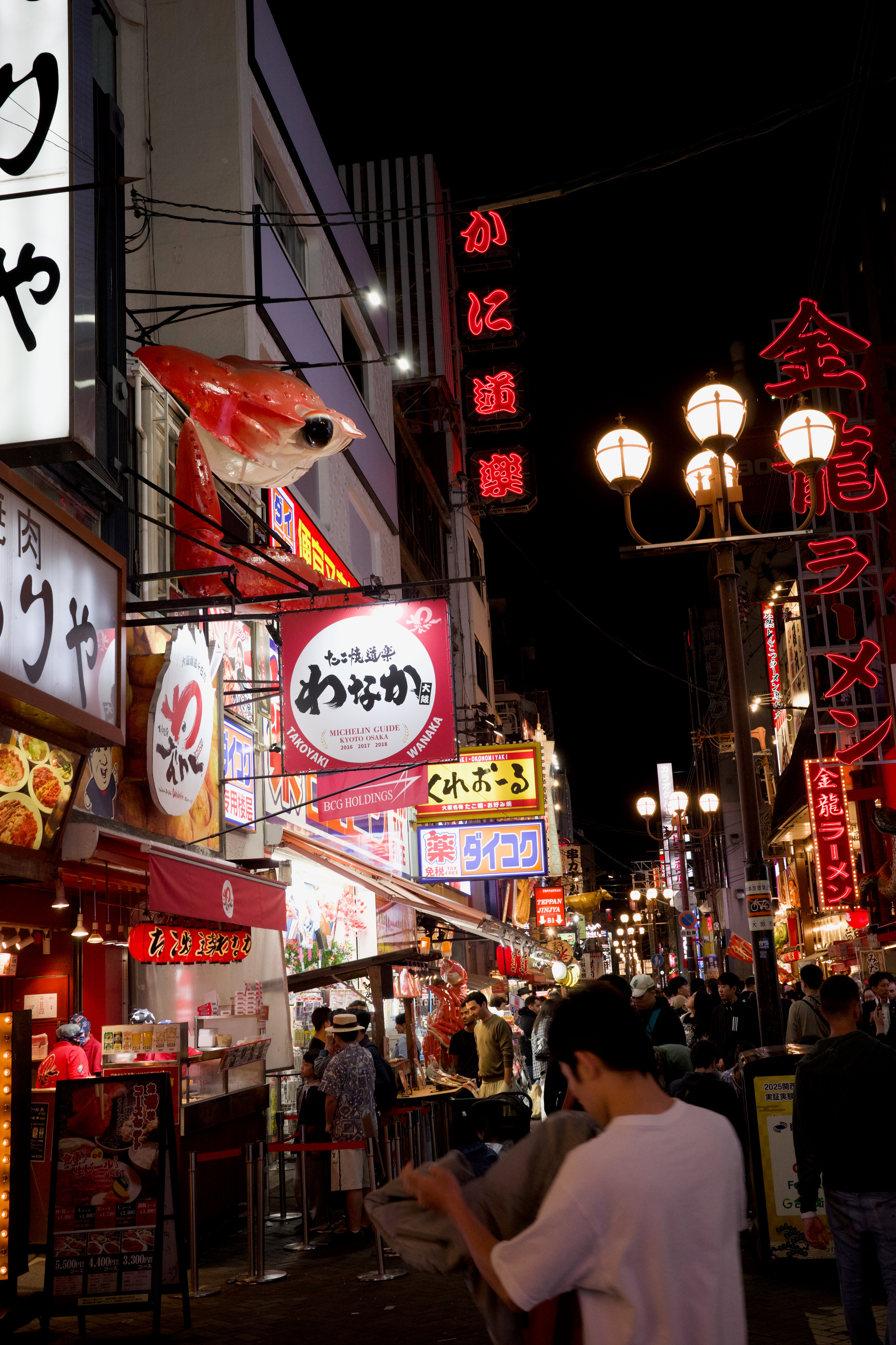 Neon signs and pedestrians fill a narrow night street.