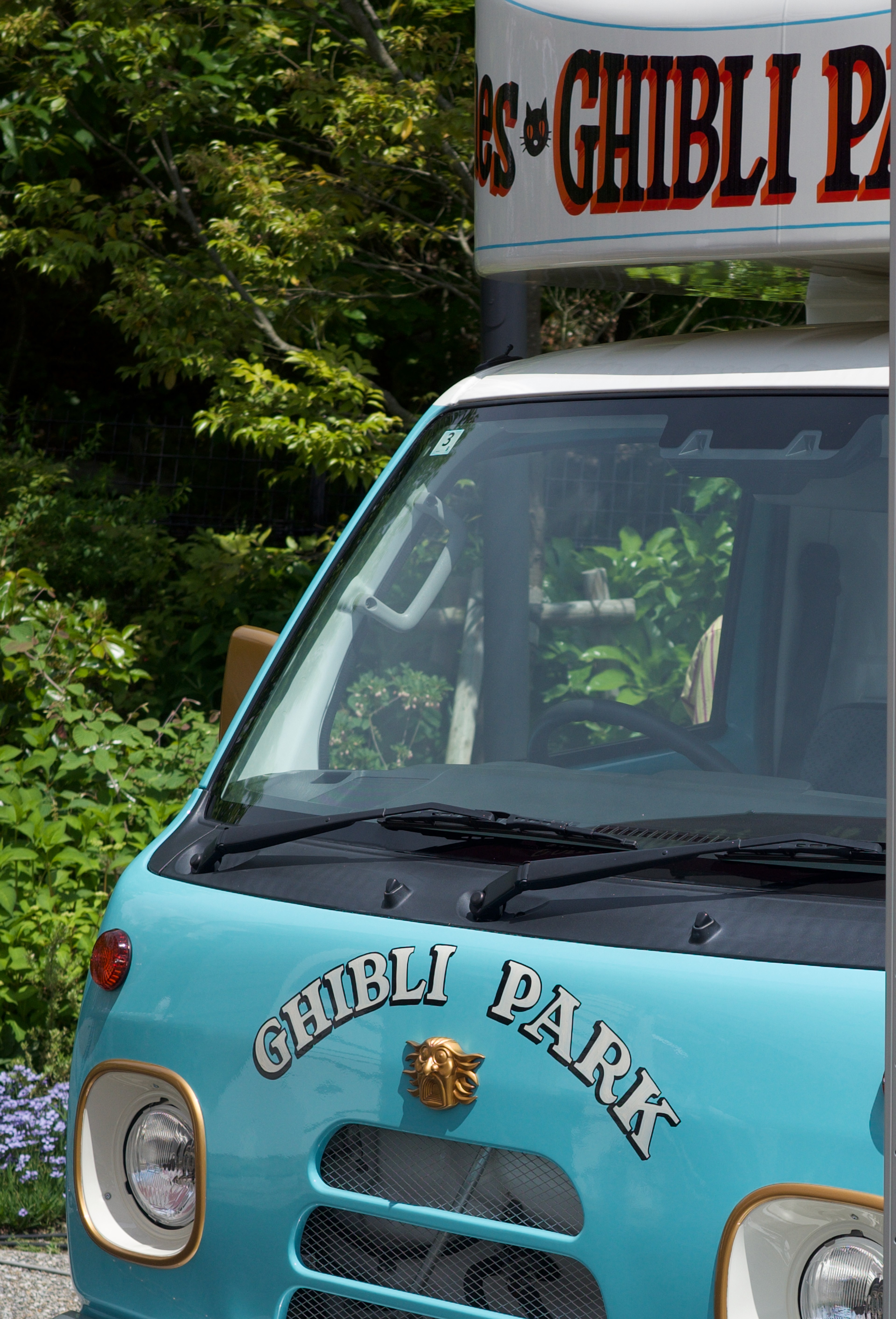 A turquoise delivery van is parked beside a wooded road.