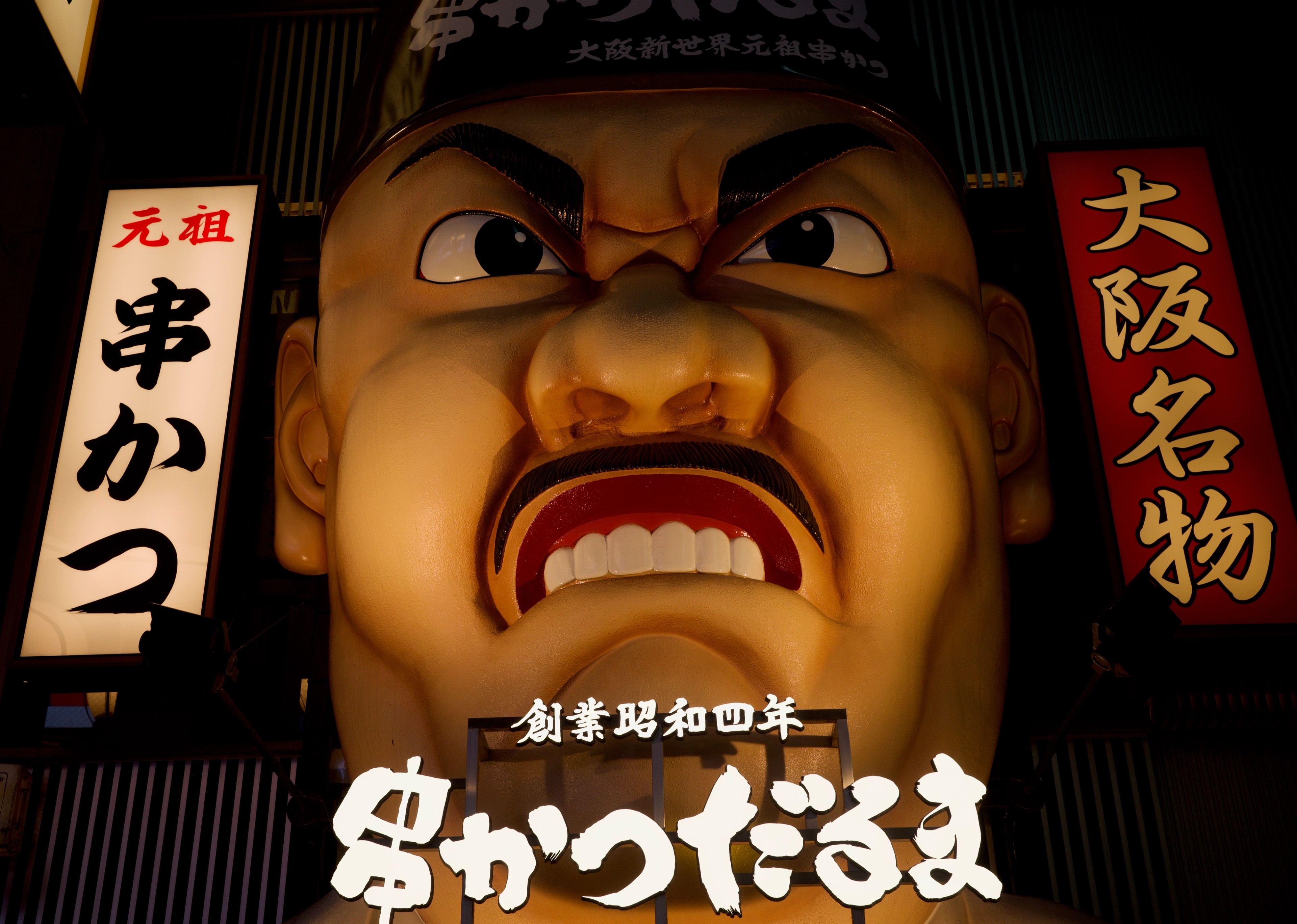 A red-faced sign hangs above a restaurant at night.