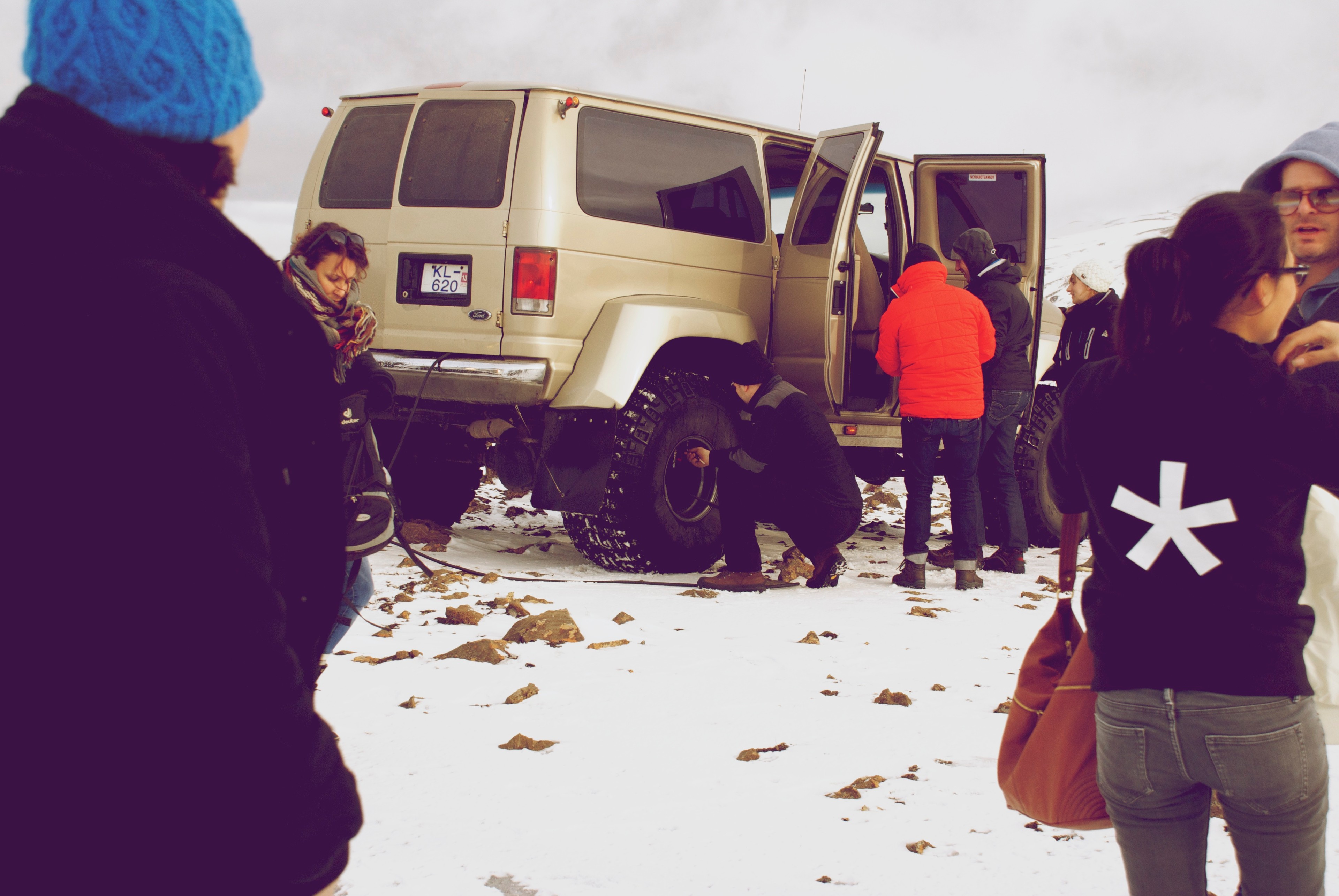 People gather beside a white four-wheel-drive vehicle on a snowy plain.