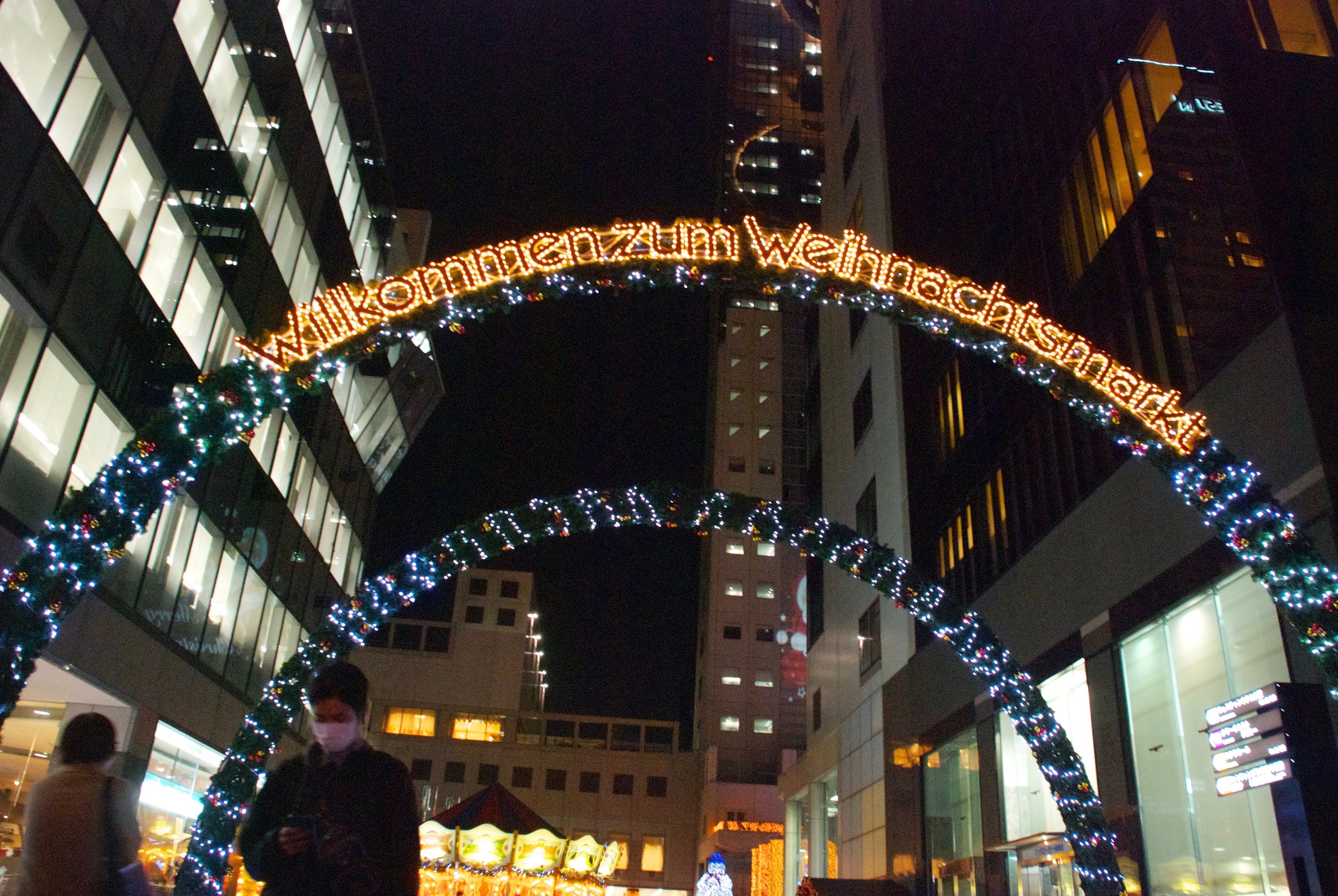A large illuminated arch spans the entrance of a city shopping district.