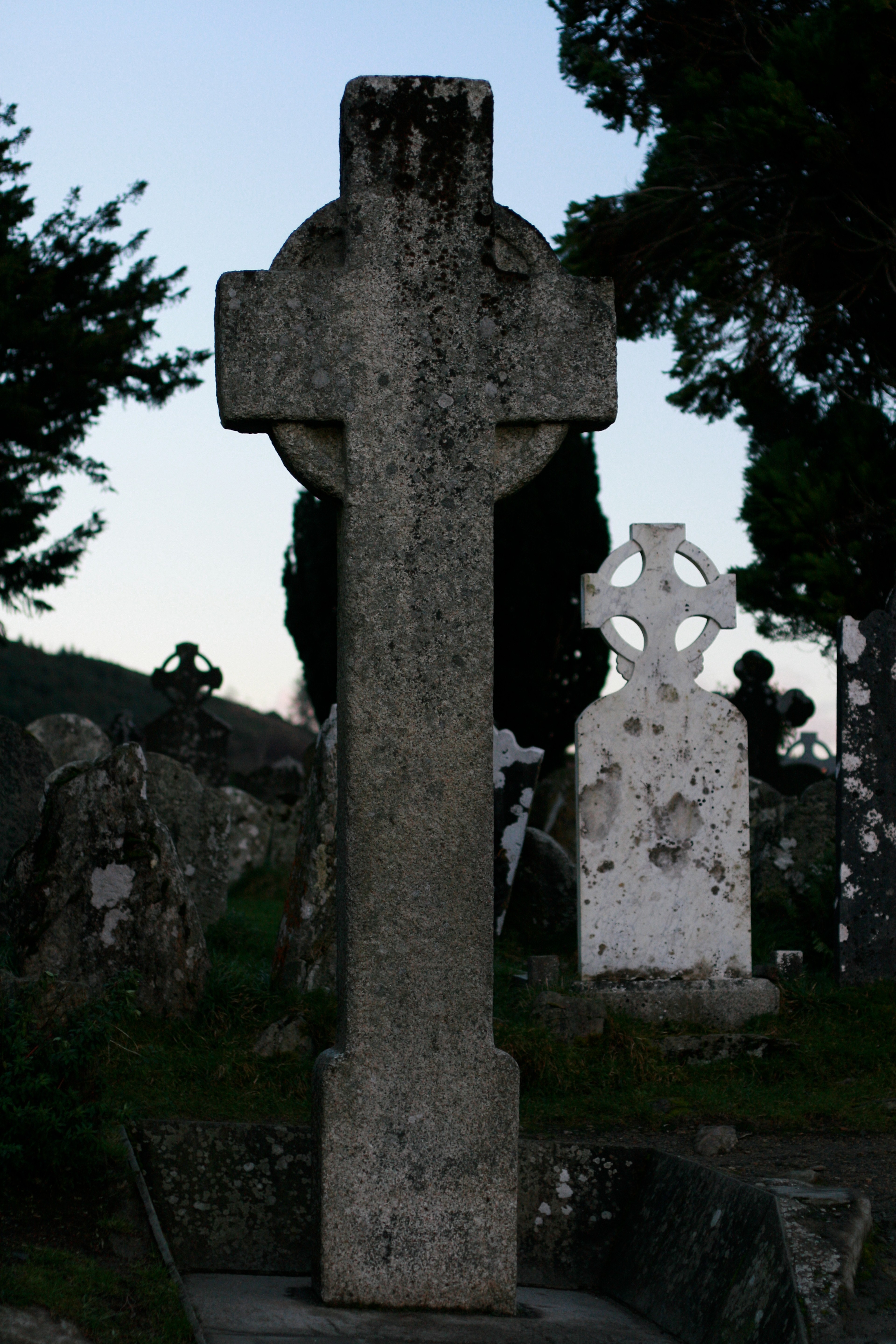 A tall stone Celtic cross stands among gravestones.