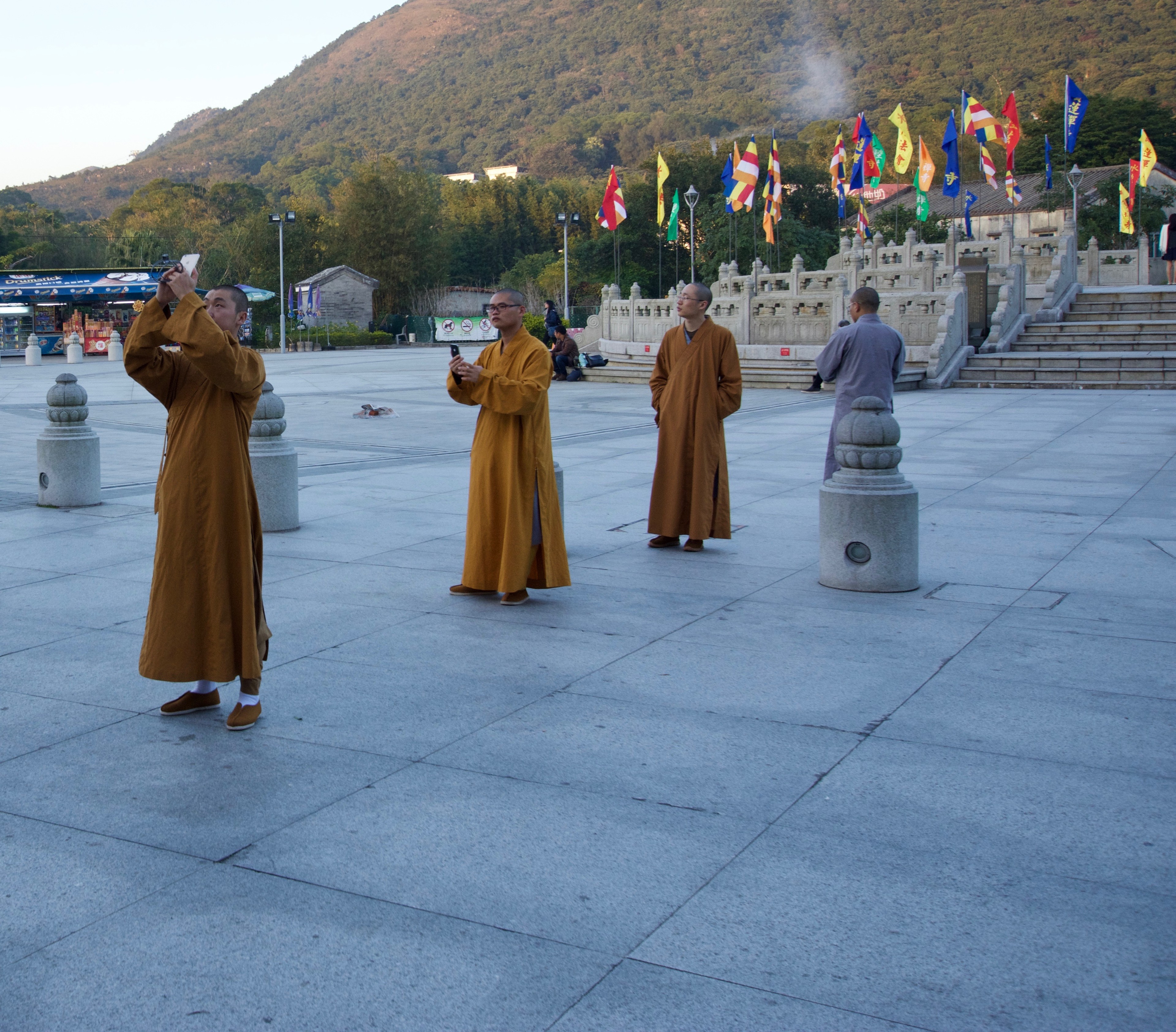 Monks in brown robes stand among statues in a broad temple courtyard.