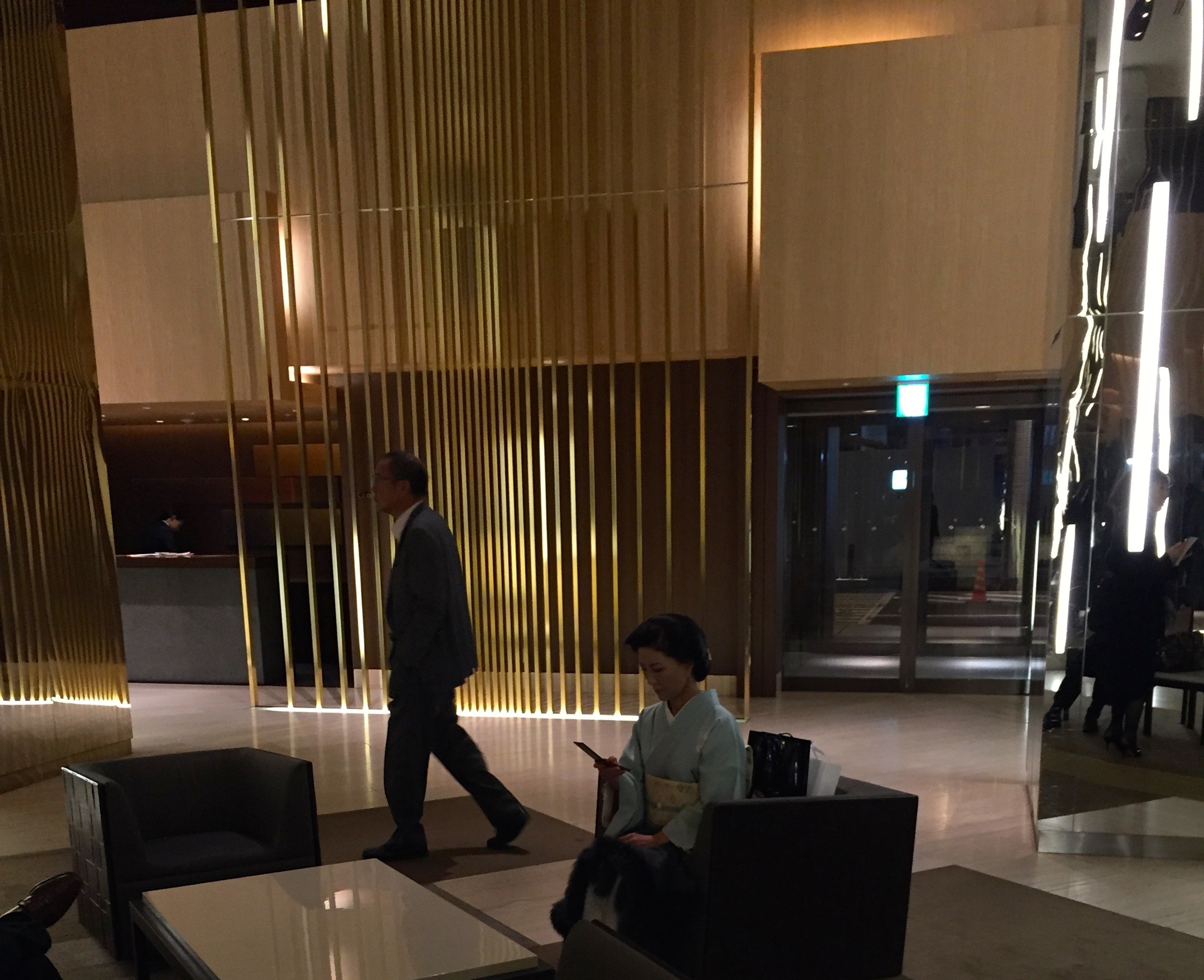 People sit and walk inside a modern lobby with a softly lit interior.