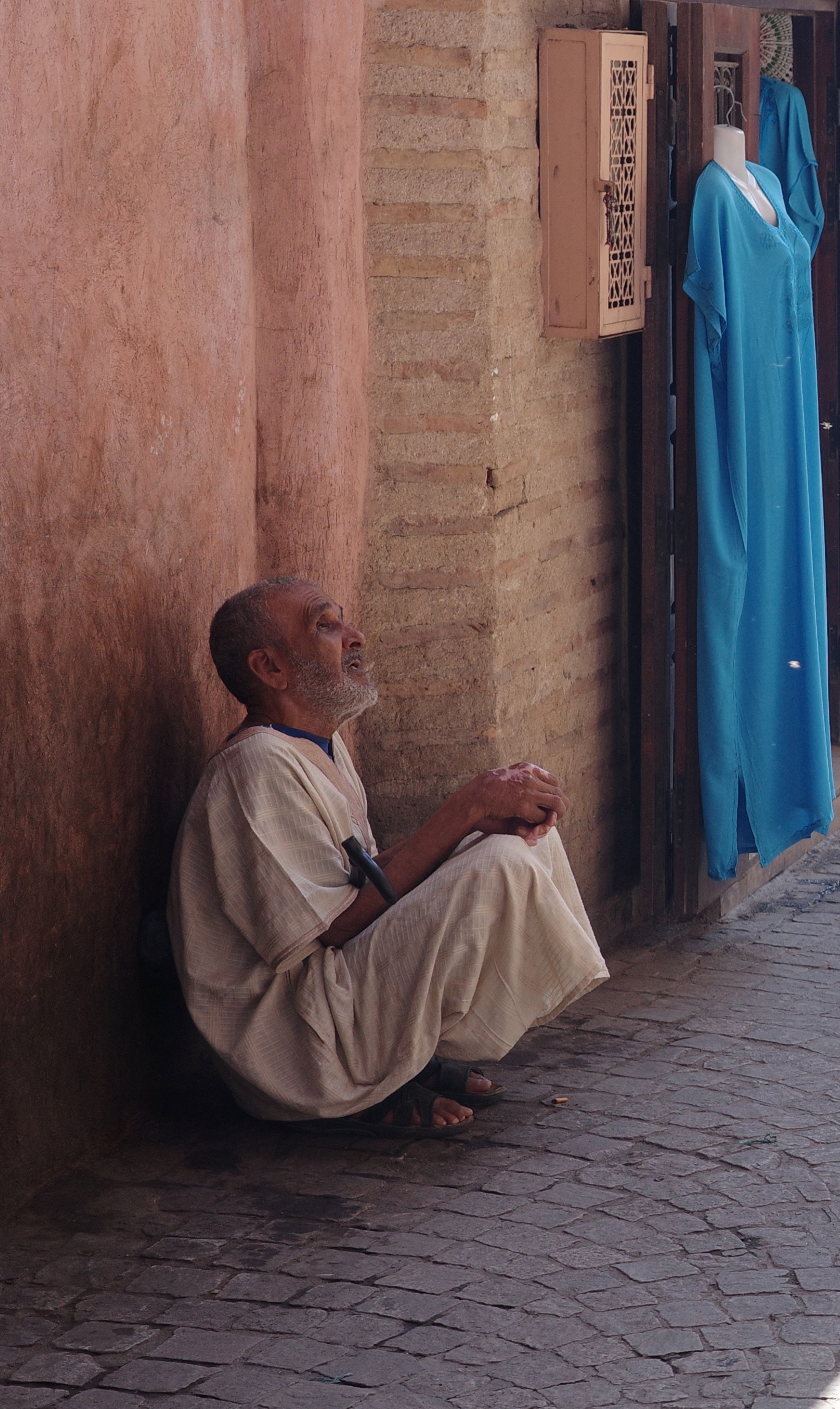 A man sits against a pink wall beside a blue hanging cloth.