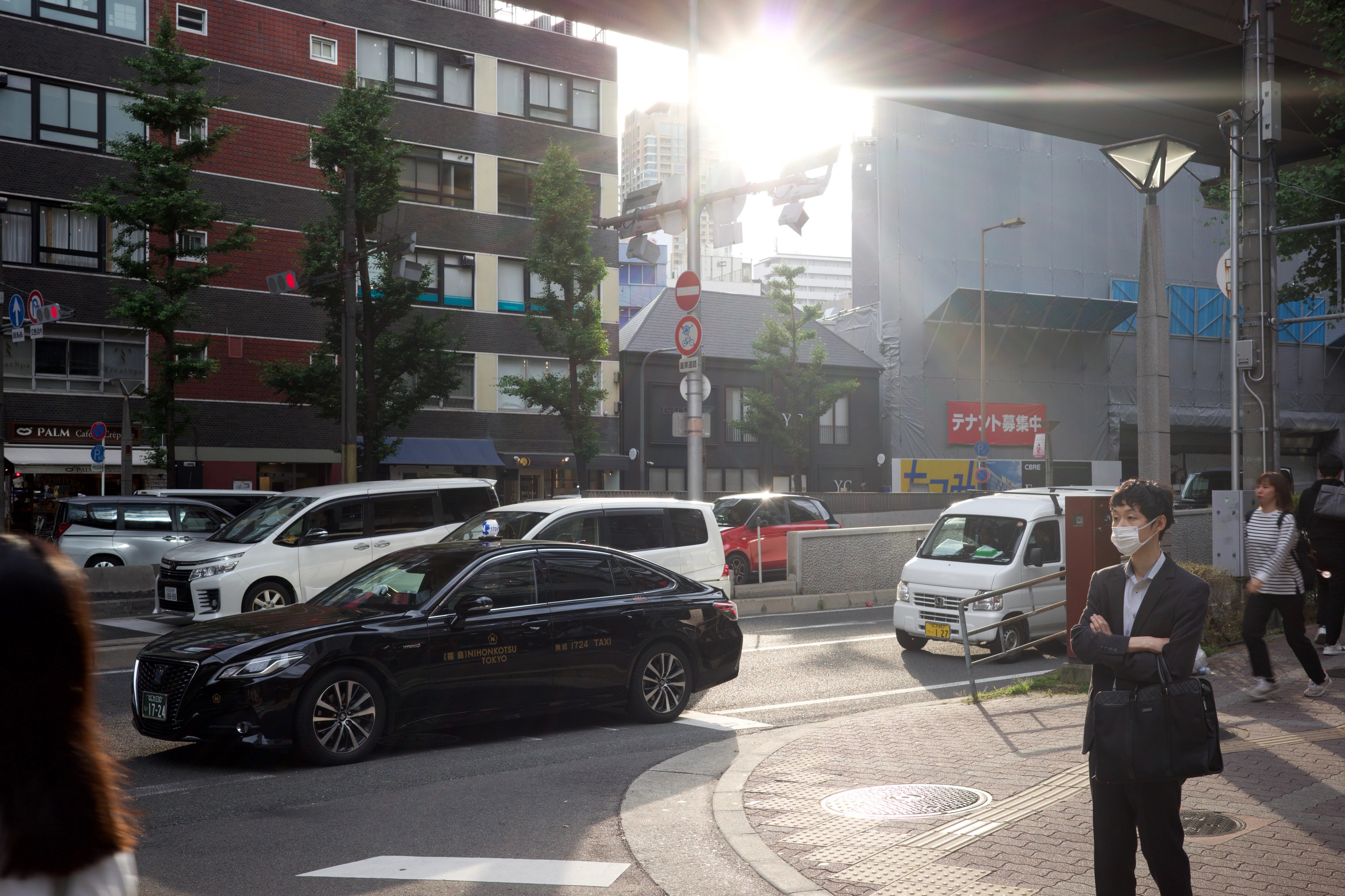 Cars and pedestrians share a sunlit street.