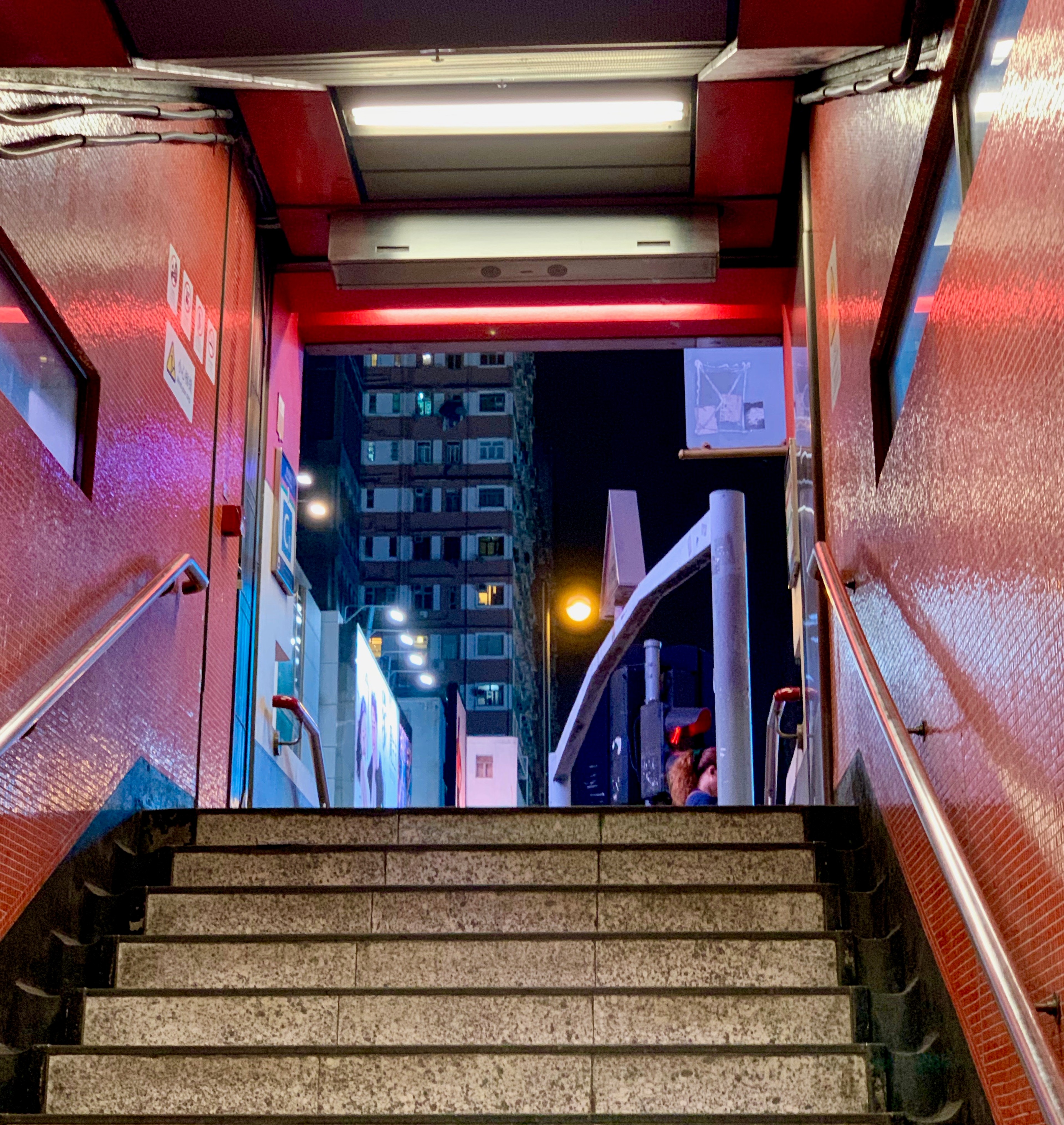 Red tiled steps descending into a Hong Kong subway station at night.
