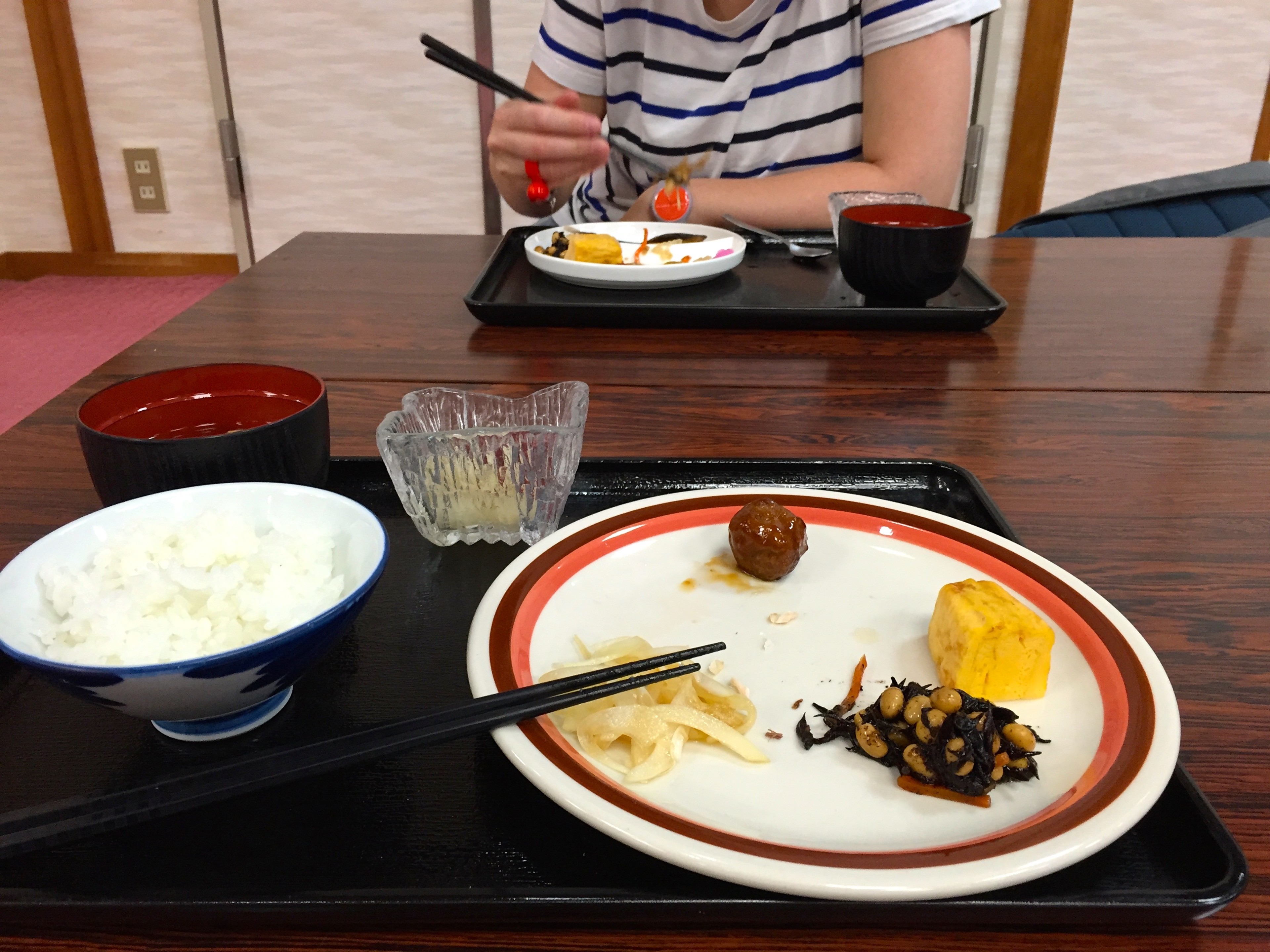 A diner serves a meal at a low table with rice, soup, and side dishes.