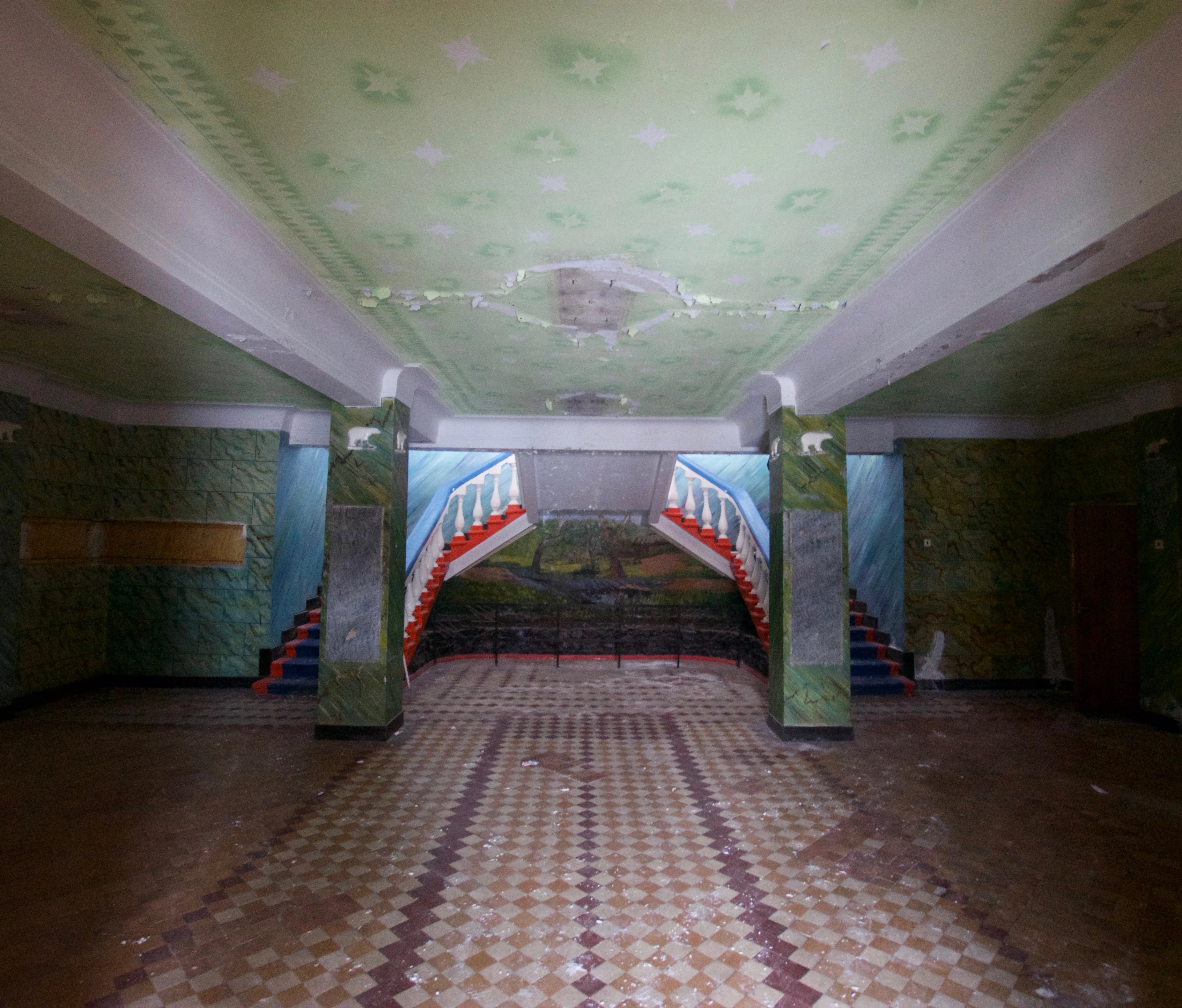 A long tiled hallway with a painted ceiling and stairway.