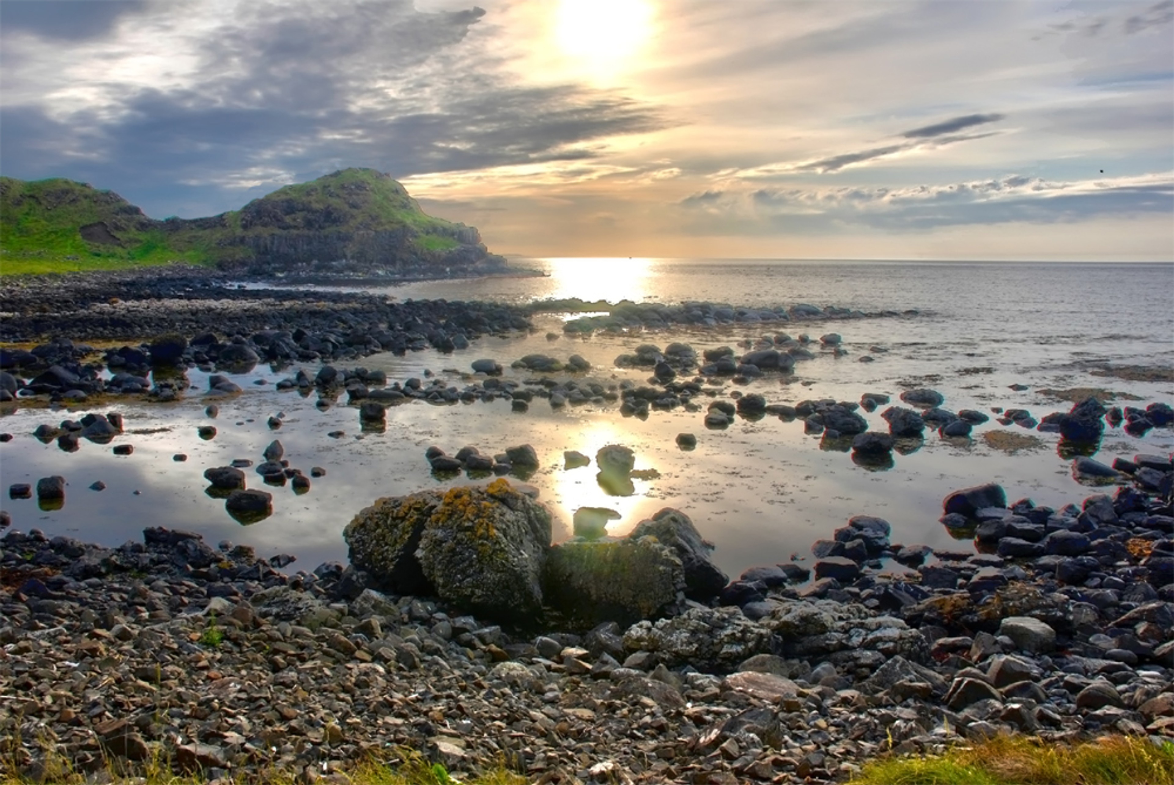 Sunlight reflects across a rocky shore beside the Giant’s Causeway.