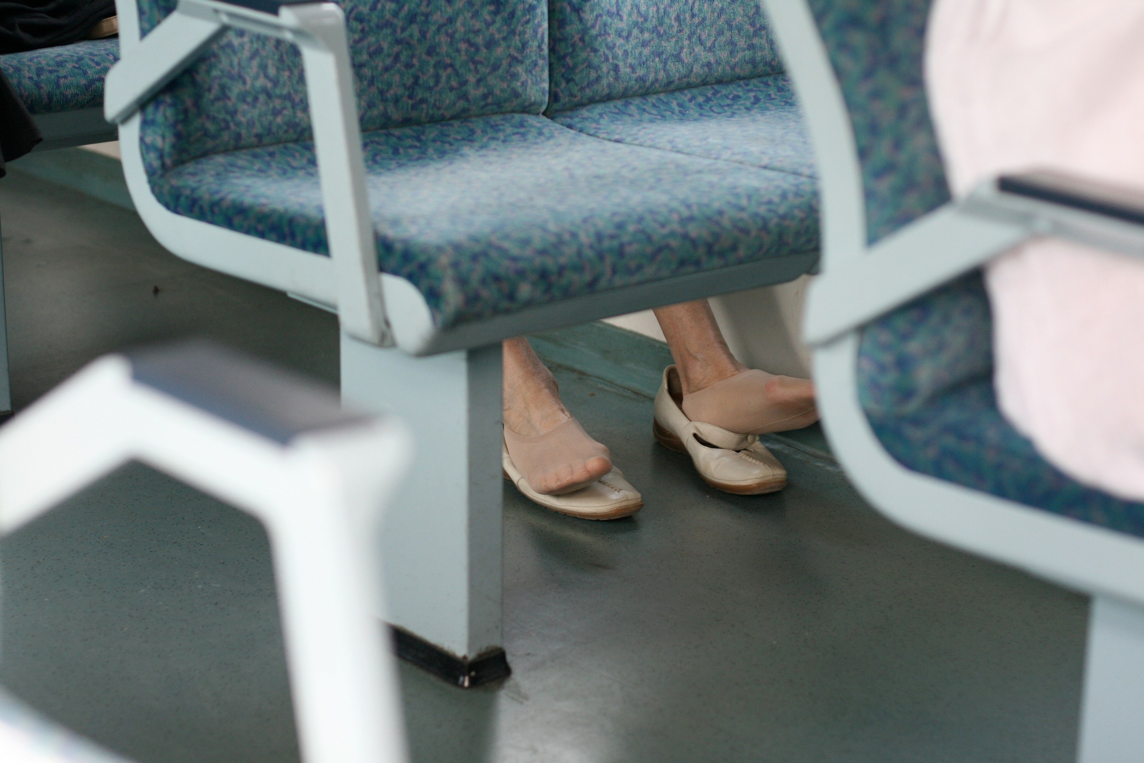 Passengers’ shoes and legs are visible beneath blue seats inside a train.
